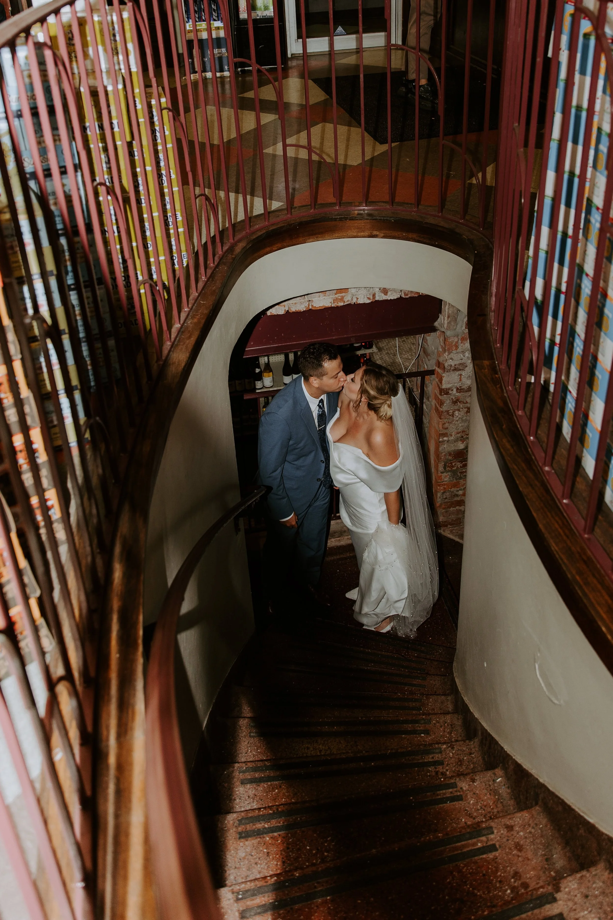 The bride and groom kiss at the bottom of a stairwell.