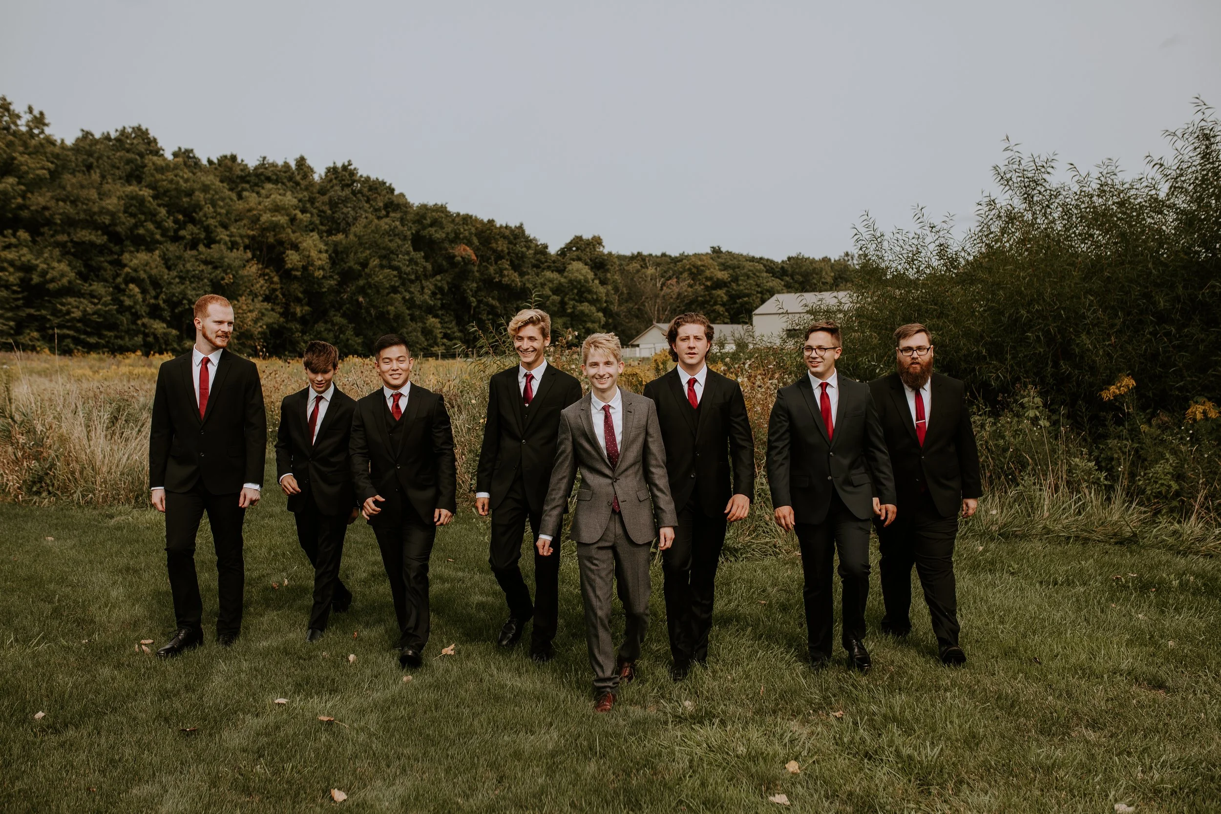 Groom walking across a field with his groomsmen, all dressed in suits and ties, ready for the wedding.