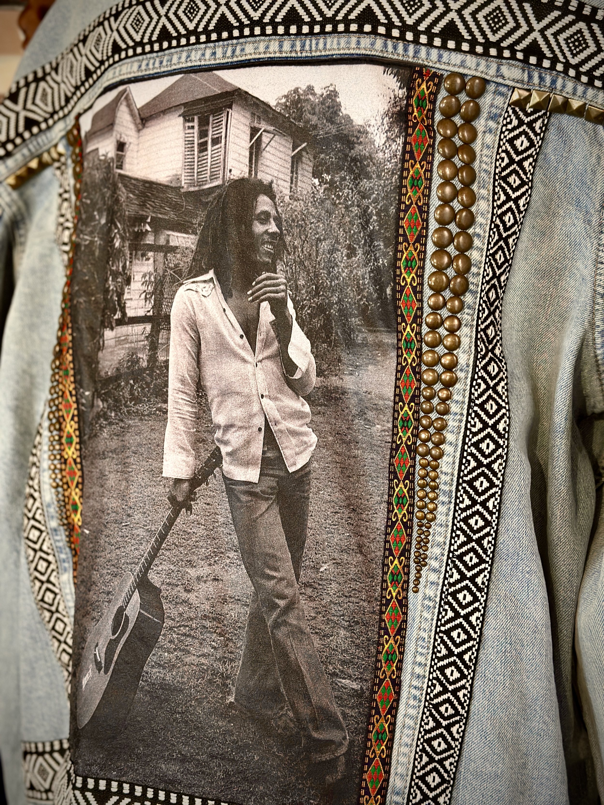 Denim jacket featuring black and white photo of a man with a guitar, embellished with ethnic patterns and decorative beads.