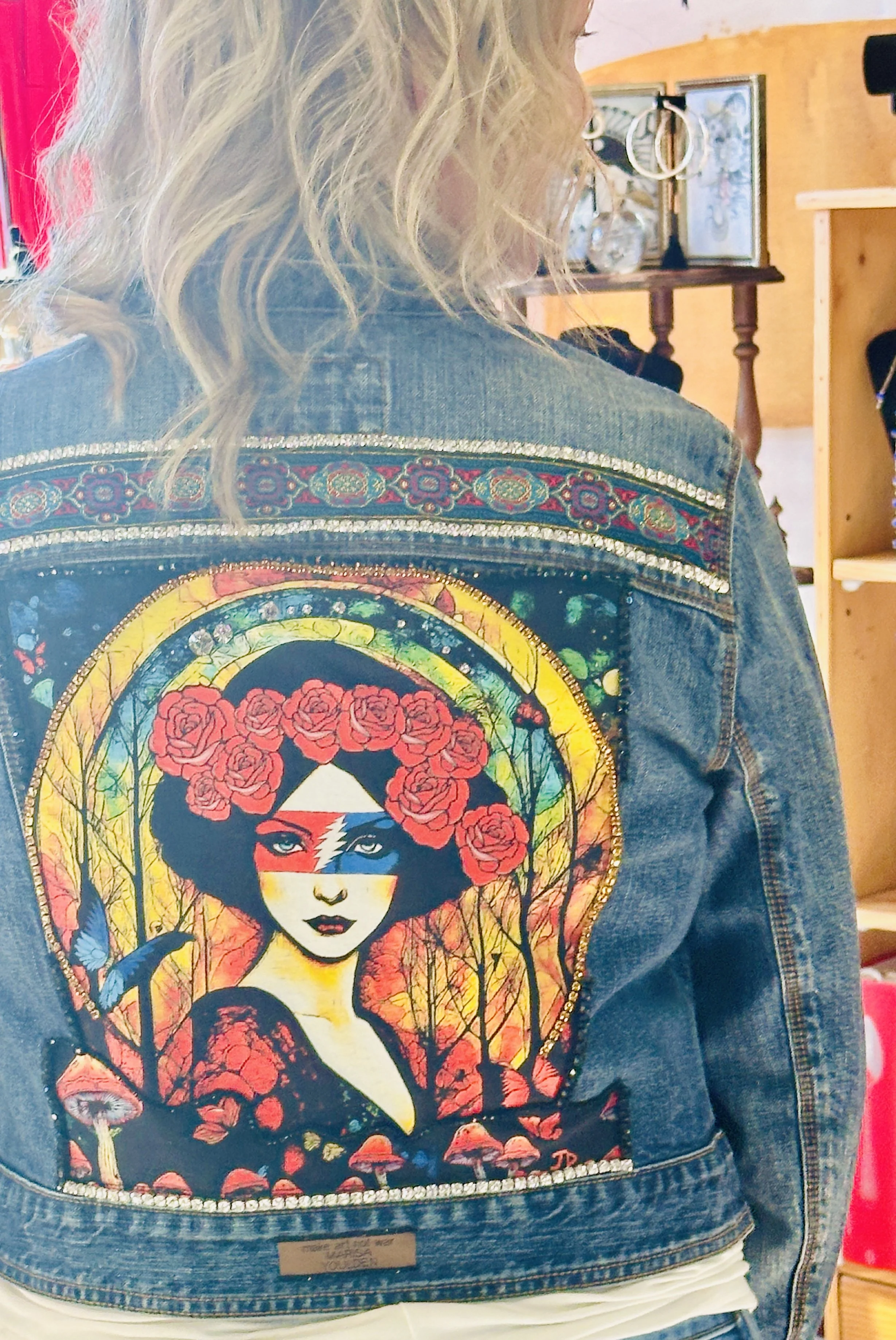 Person wearing a denim jacket with colorful artwork of a woman adorned with roses and vivid background.