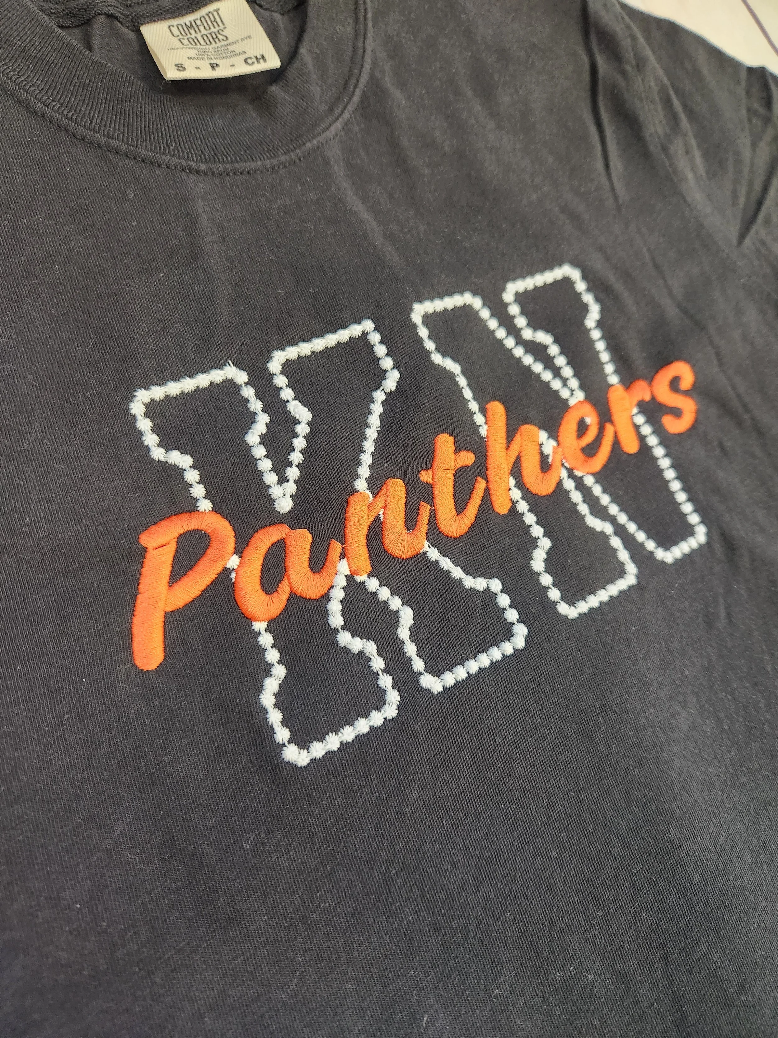 Embroidered KN Panthers Comfort Color T-Shirt, black t-shirt with letters K and N embroidered in white thread with Panthers embroidered on top of the letters in orange thread, Knob Noster Panthers