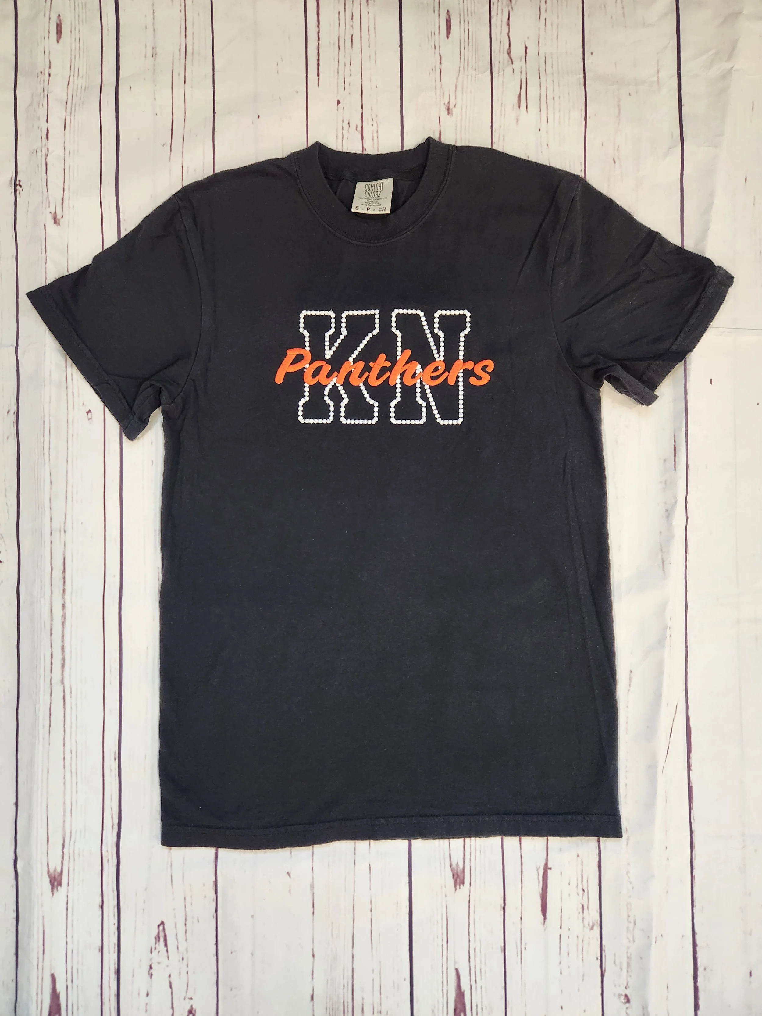 Embroidered KN Panthers Comfort Color T-Shirt, black t-shirt with letters K and N embroidered in white thread with Panthers embroidered on top of the letters in orange thread, Knob Noster Panthers