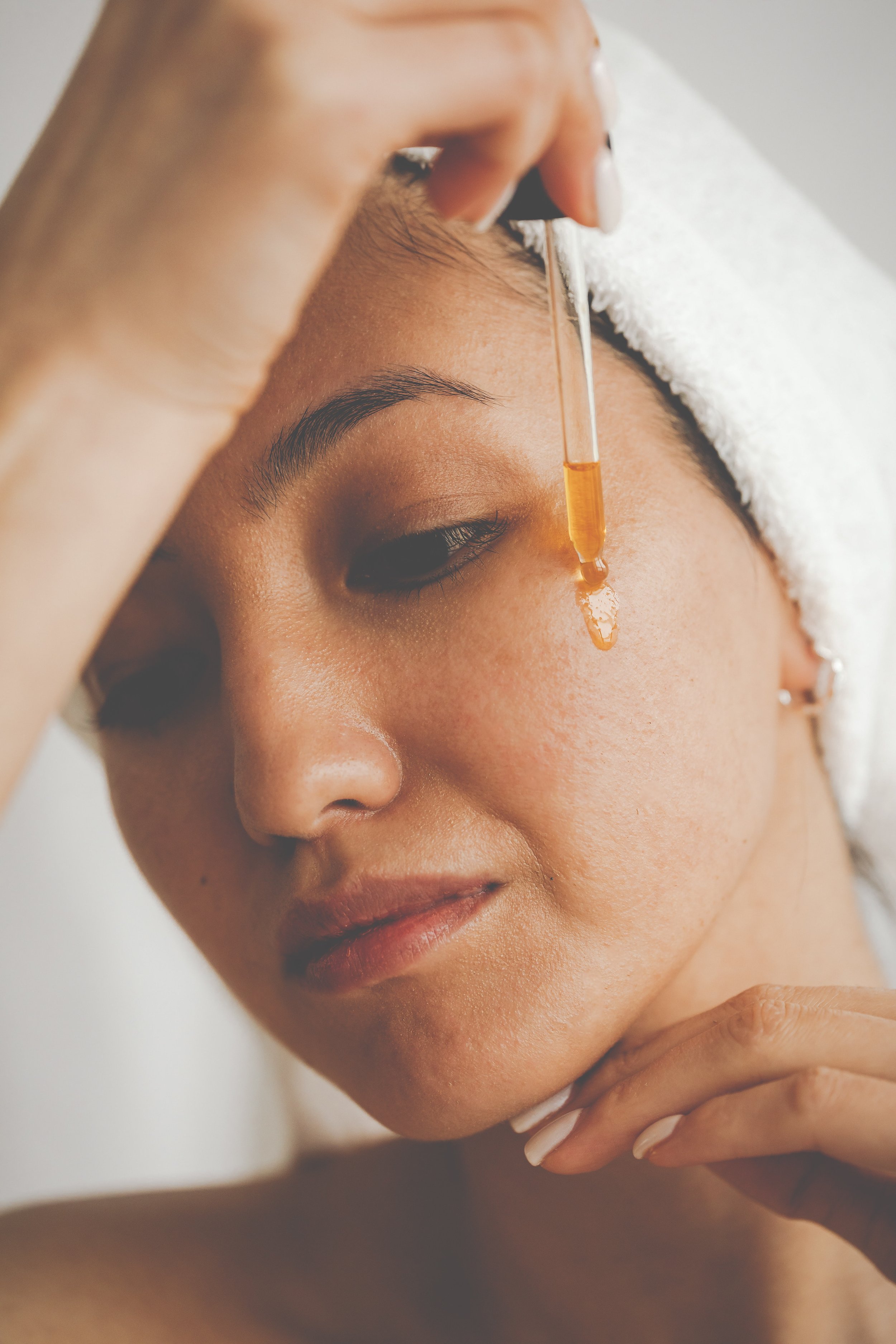 A woman applying an eyedropper of bakuchioil oil from bloom fresh skincare to her face.