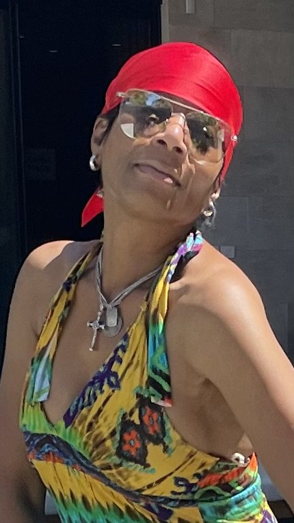 A woman in a yellow dress and glasses standing outside in the sunlight.