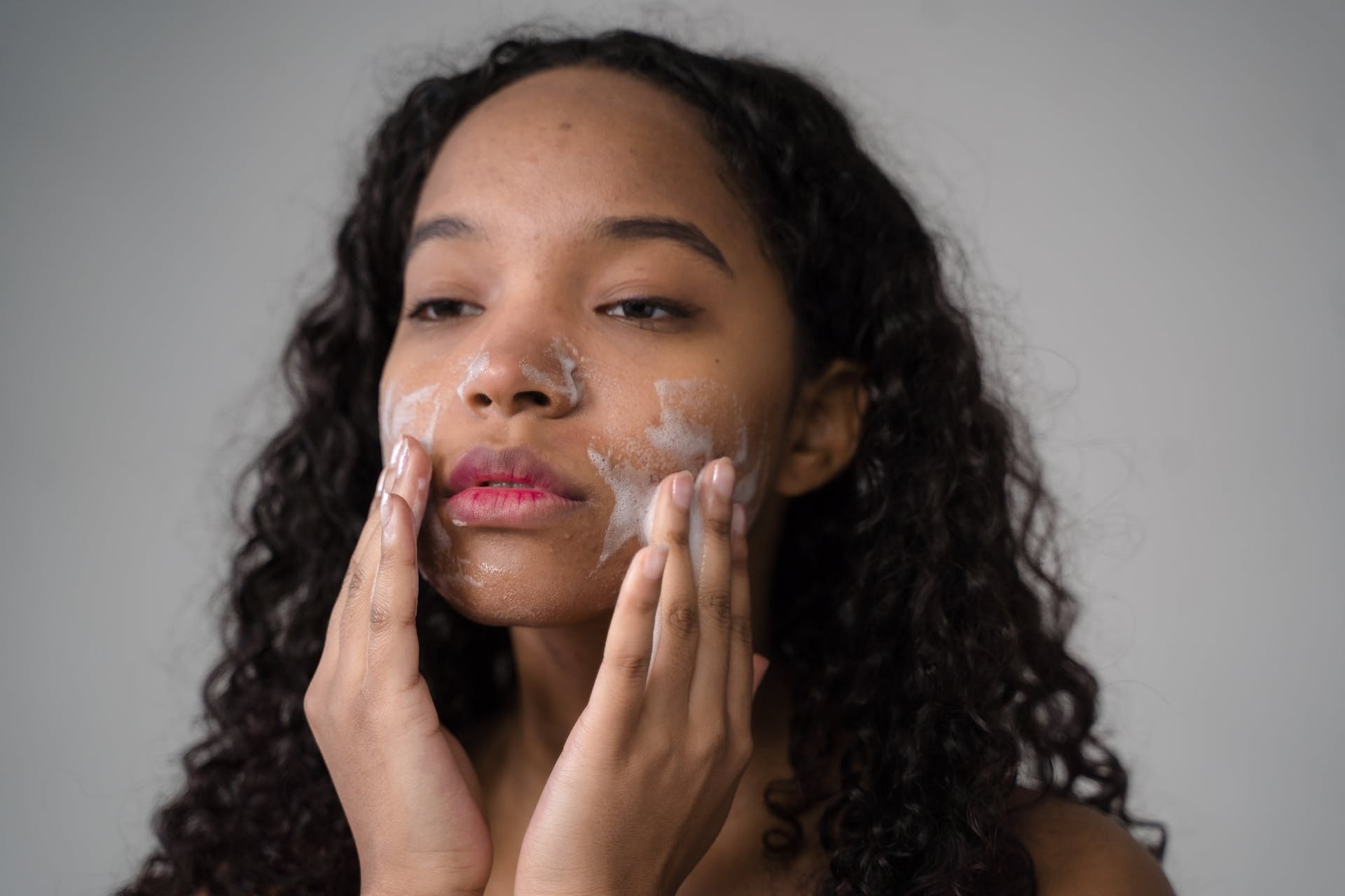 A woman applying radiant renewal facial cleanser from bloom fresh skincare to her cheeks.