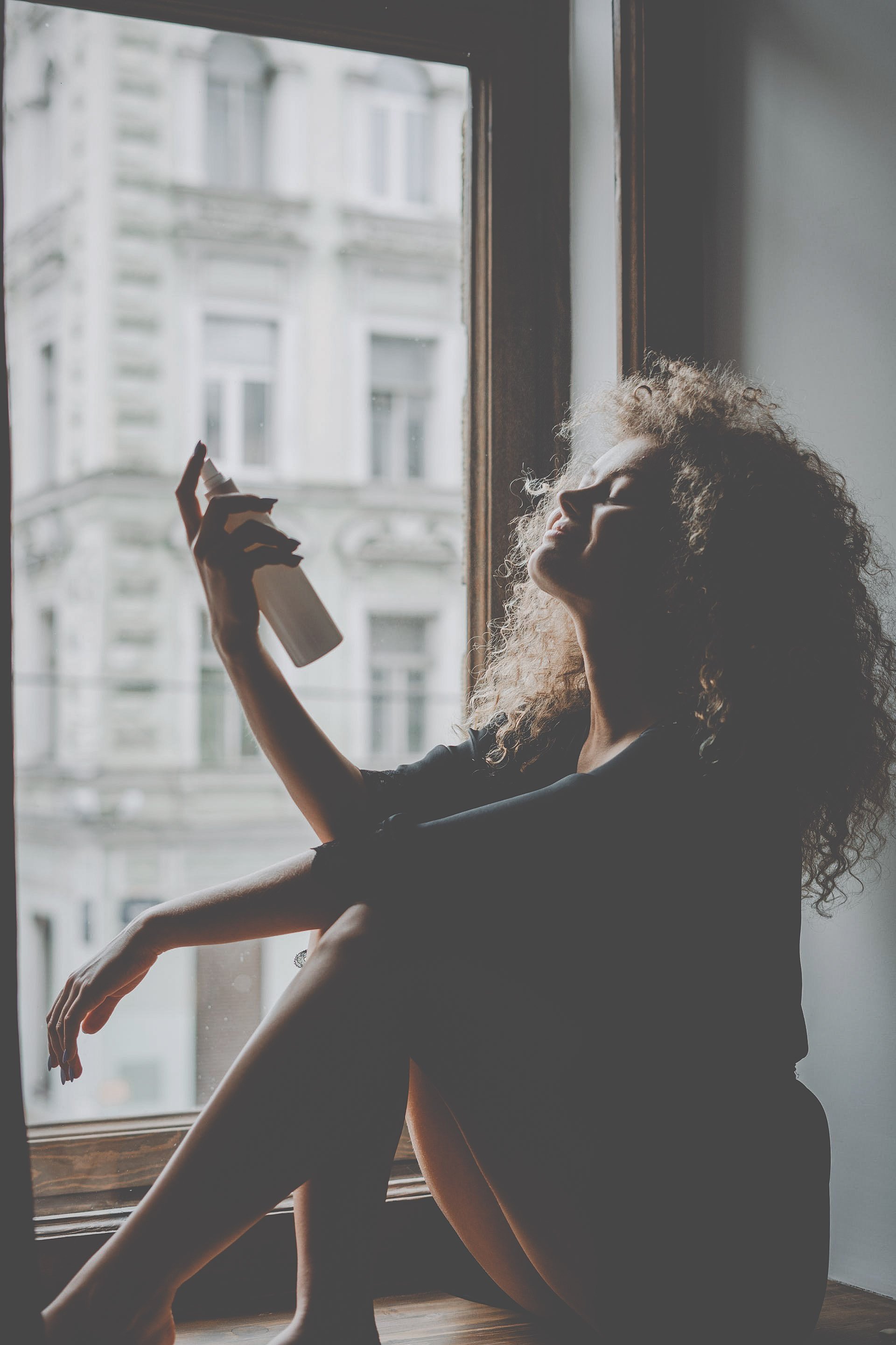 A woman sitting next to a window misting herself with dewy rose hydration toner. (Copy)