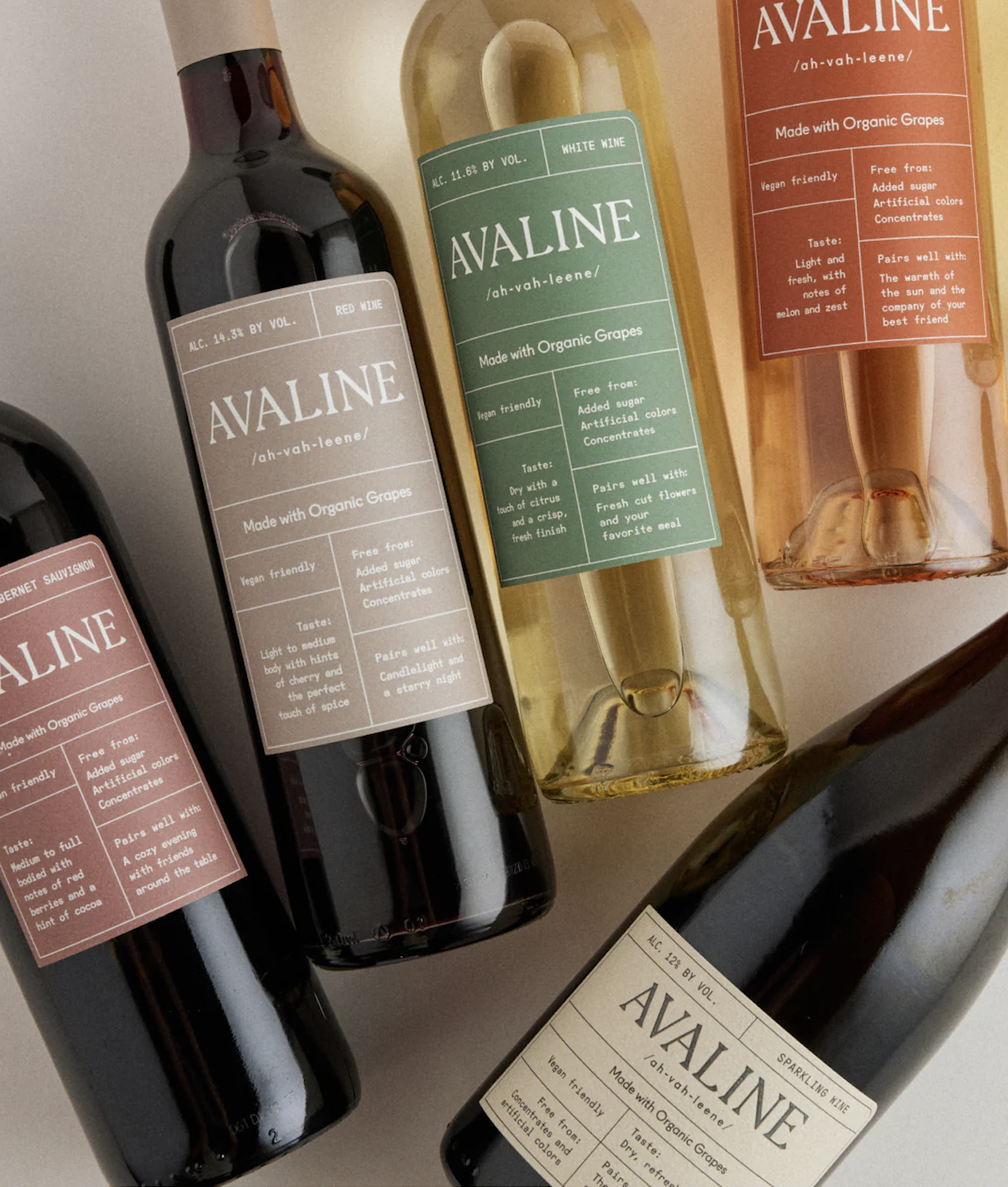 Multiple bottles of Avaline wine in various colors with labels displaying the brand name, alcohol content, and descriptions. The bottles include red, white, pink, and sparkling varieties, placed on a neutral surface.