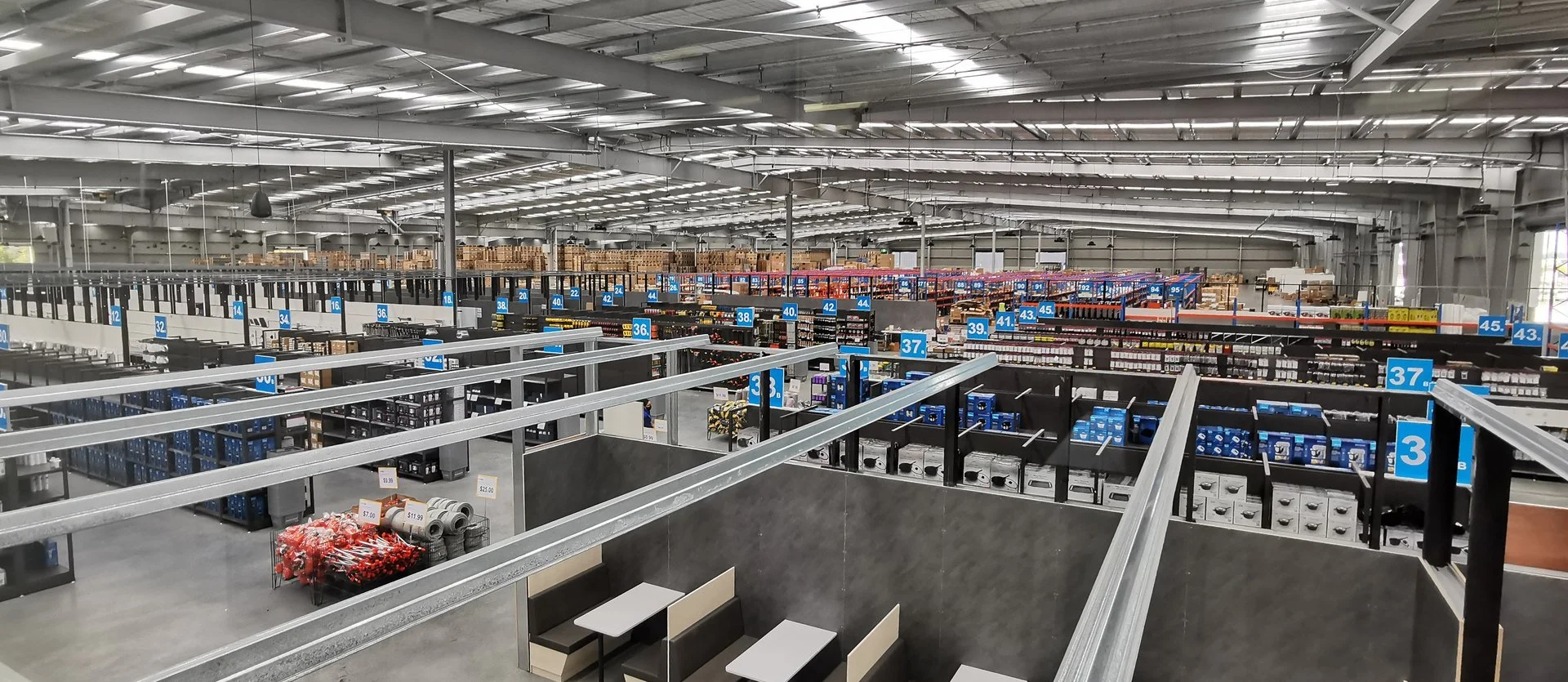 Empty warehouse or large retail store with organized shelving units and blue numbered signs, some furniture near the front.