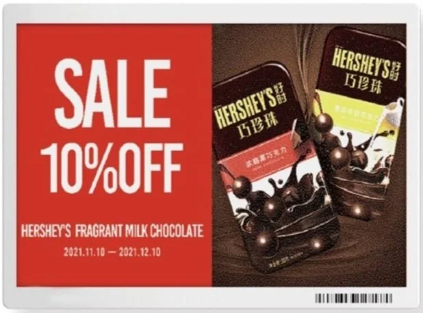 Hershey's fragrant milk chocolate sale sign offering 10% off, with images of Hershey's chocolate bars, one with a pink label and the other with a green label, on a dark wooden surface.