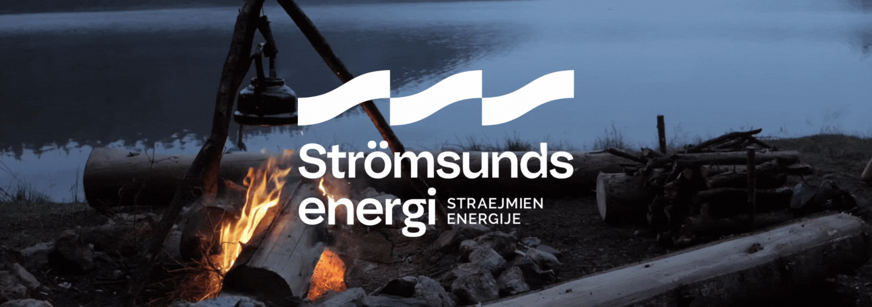 En lägereld vid en sjö eller flod med träd och stenar runt omkring. En logg brinner och det finns ett tältstativ med en lykta hängande. Logo och text över bilden: 'Strömsunds energi' på svenska, engelska, och andra språk.