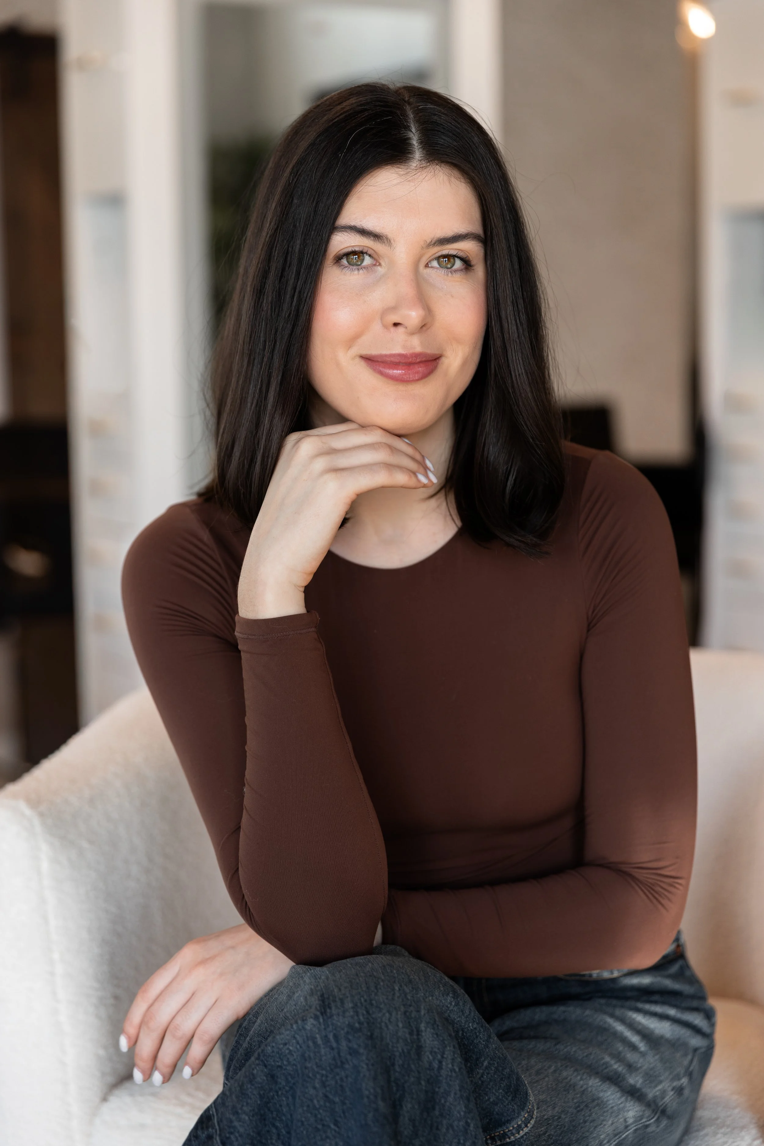 Woman applying nude lipstick while looking at herself in a compact mirror.