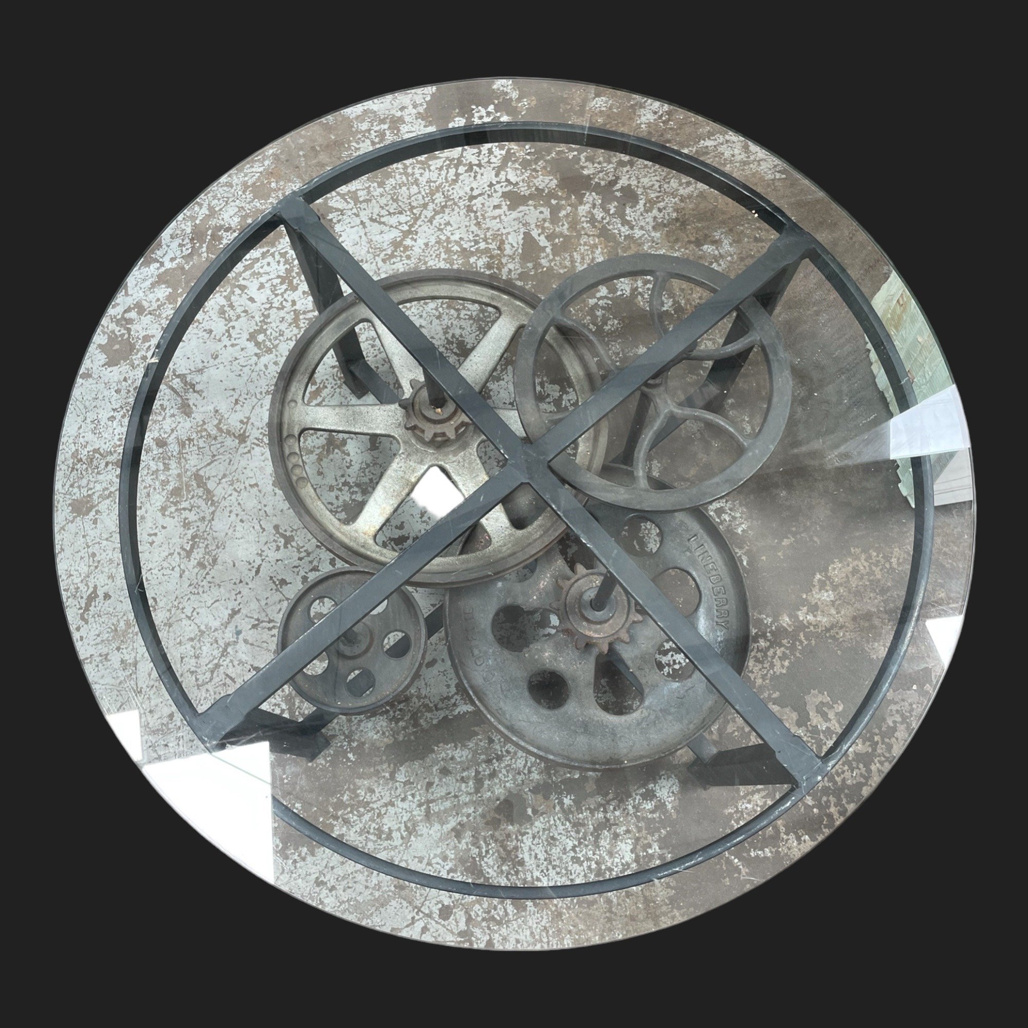 Round coffee table with reclaimed iron gears under clear glass top and black steel frame