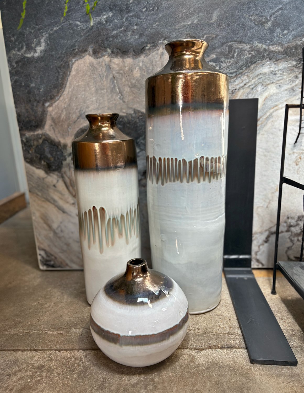 Set of three painted brass and ceramic vases in varying sizes, displayed on concrete flooring