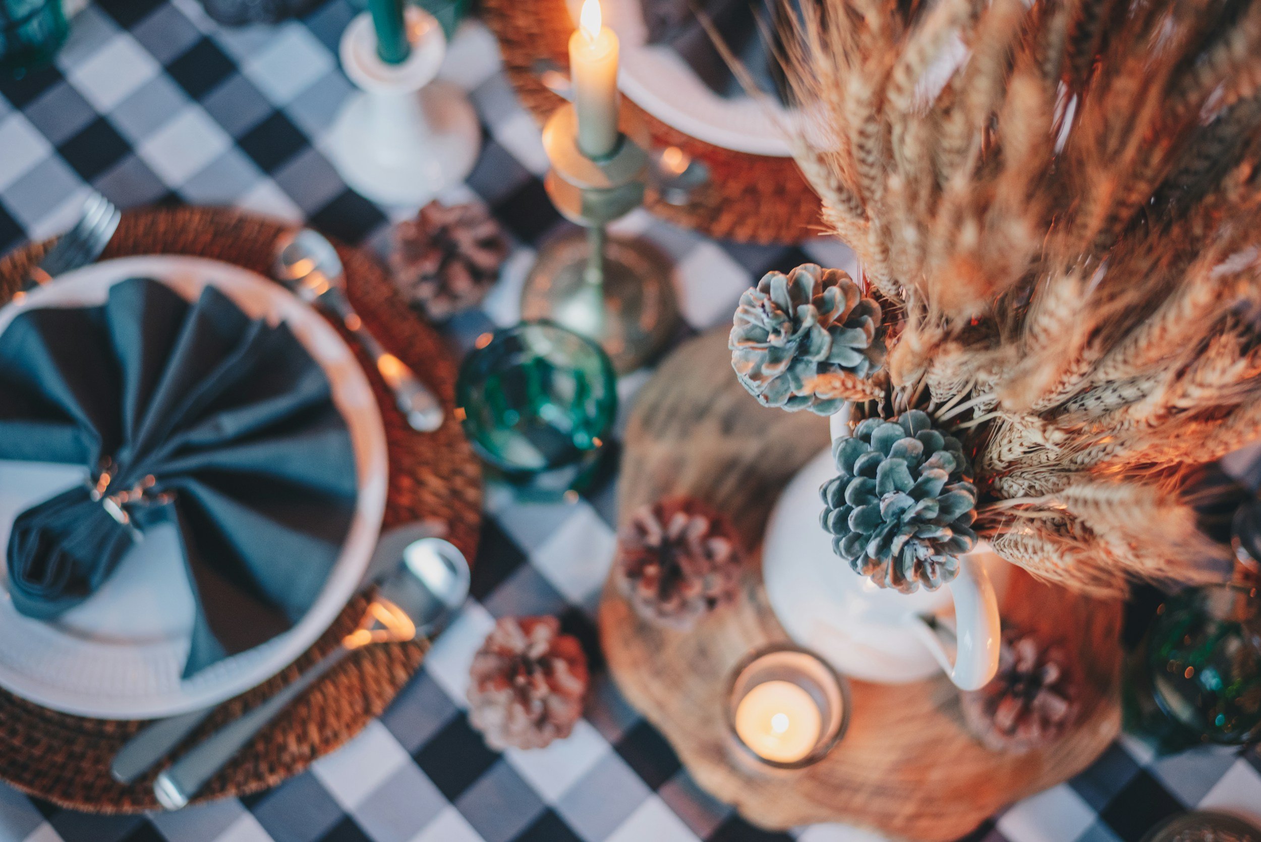 A checkered black and white table cloth featuring an array of candles, pine cones, and wooden trays holding festive fronds.
