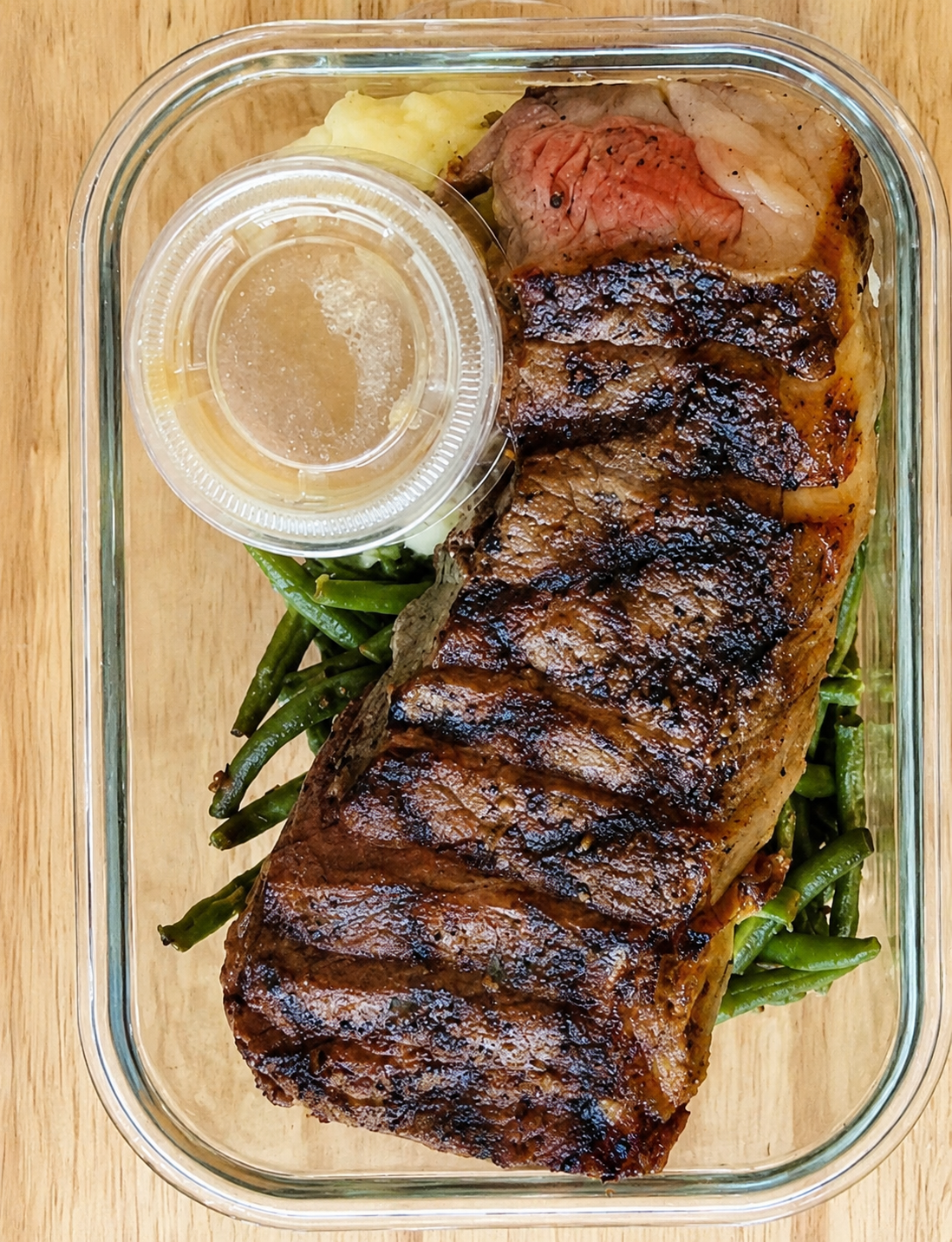 Sliced grilled steak with green beans, rice and sauce in a reusable glass container.