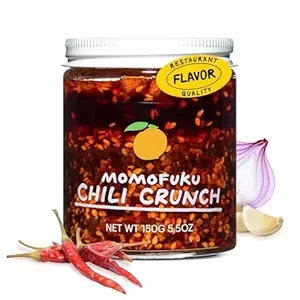 A jar of Momofuku Chili Crunch with chili peppers, garlic, and red chili peppers displayed next to it.