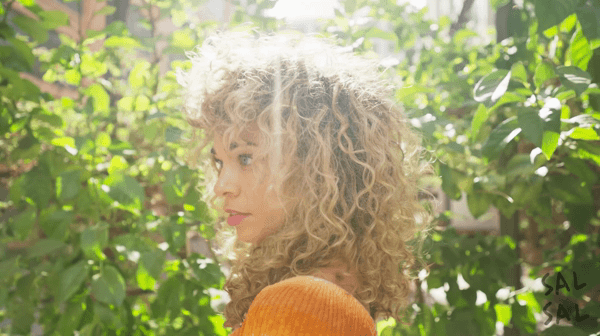 Voluminous blonde curly haircut with face-framing bangs and defined natural curls, styled by Sal Salcedo.