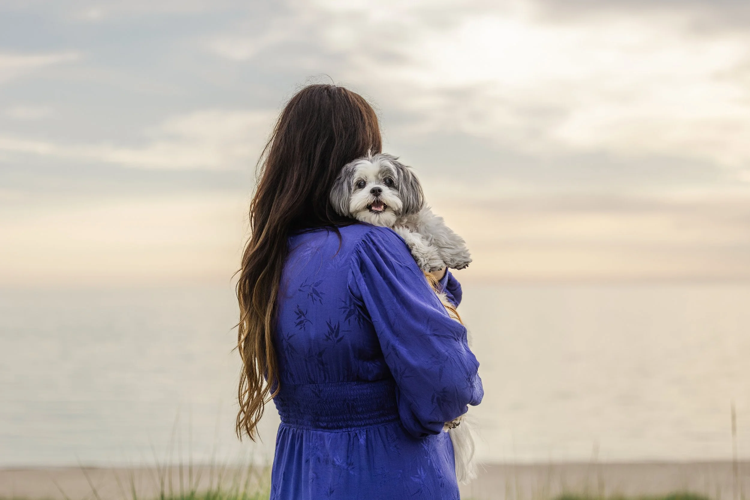 Woman holding small dog at sunset on Northern Michigan beach, emotional dog and owner portrait