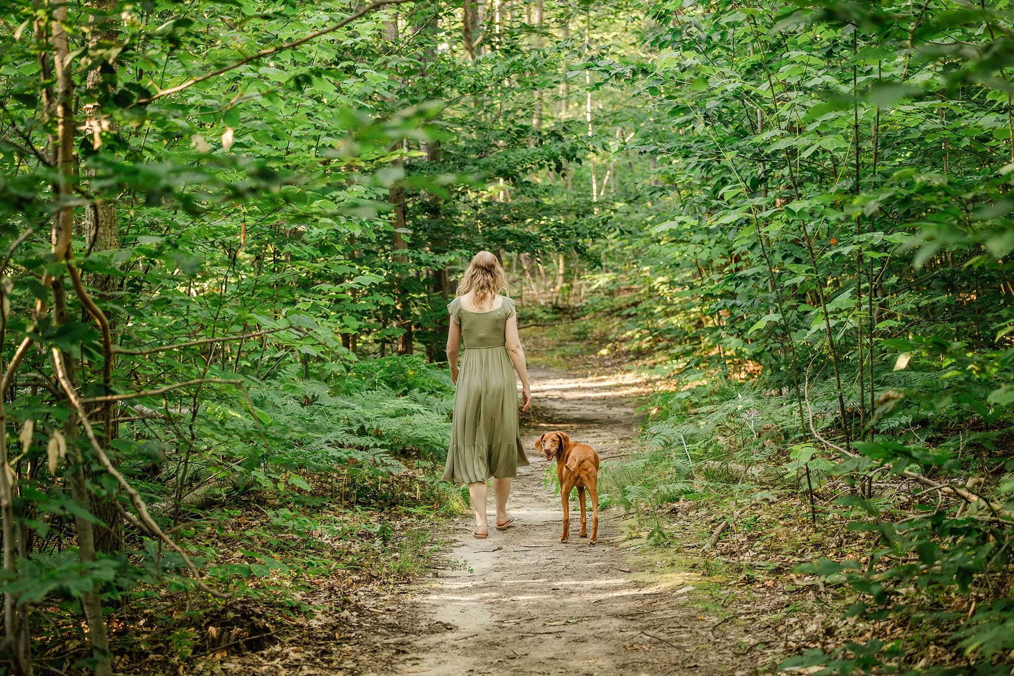 Woman and dog walking Northern Michigan trail together, candid moment during pet photography session