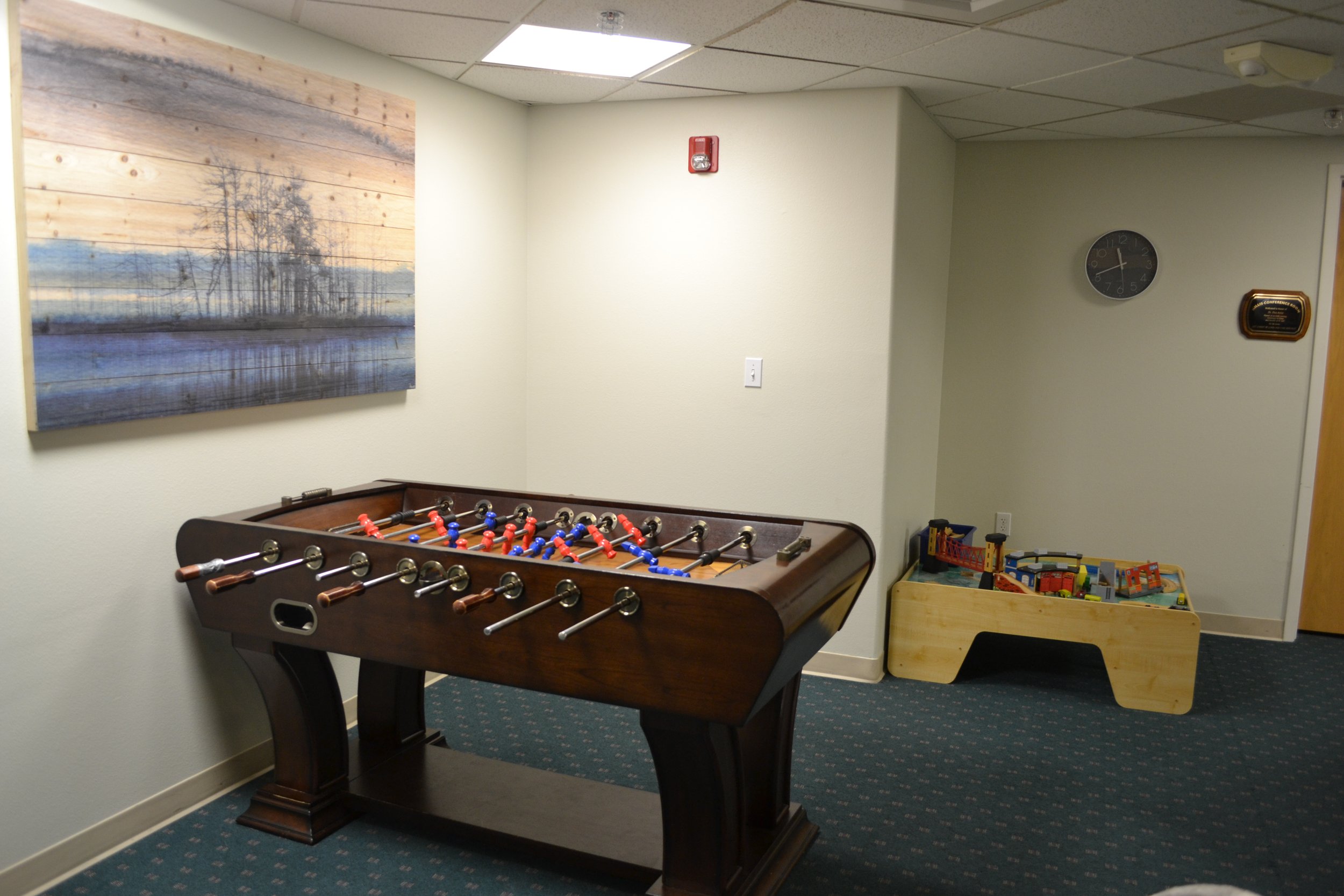 Room with a foosball table, wall art, toy train set, and clock.