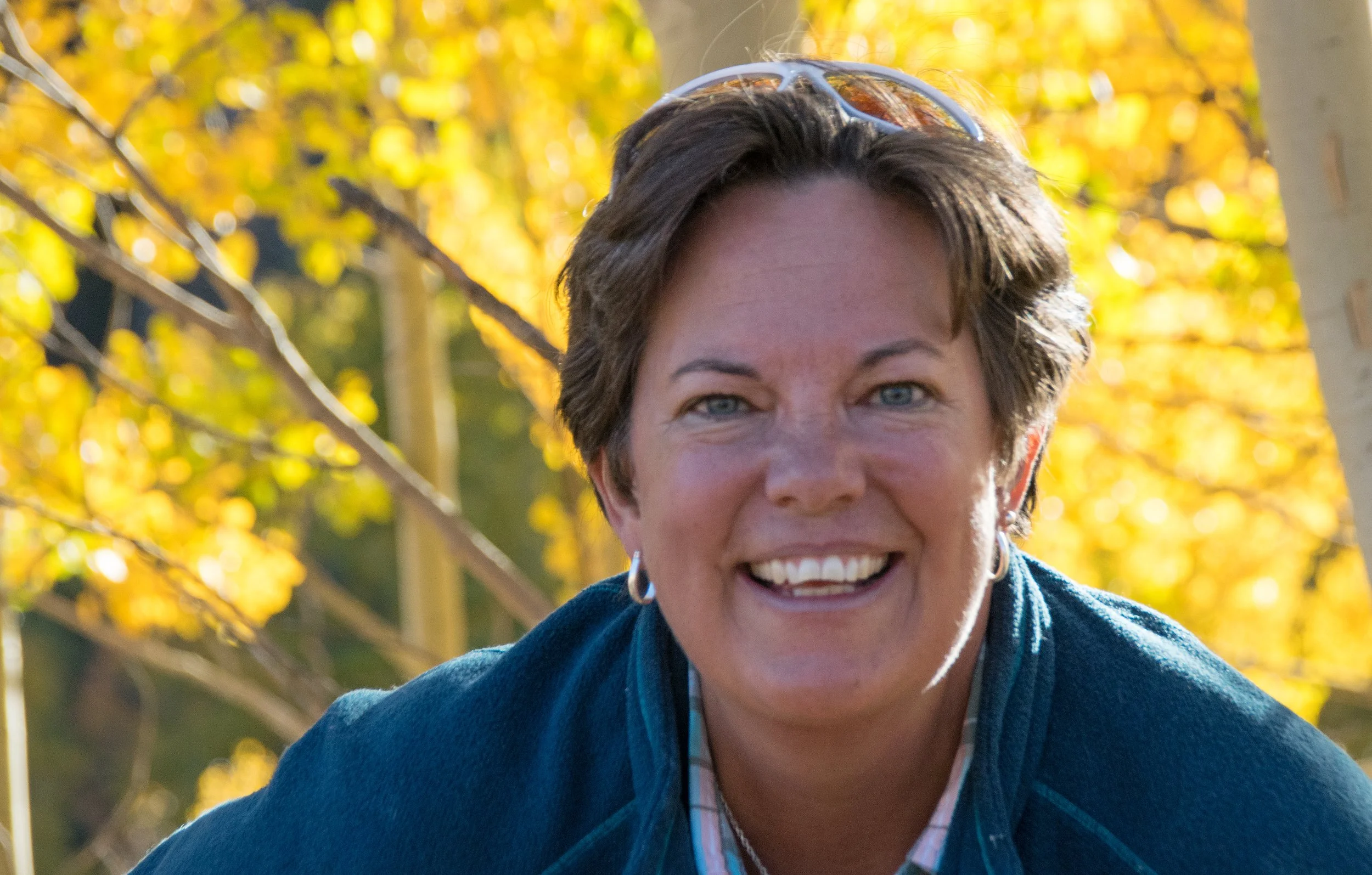 Smiling person in outdoor setting with autumn foliage.
