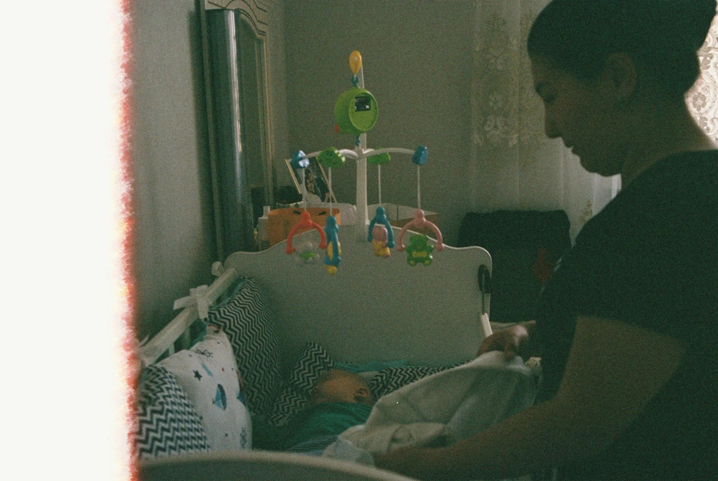 tired parent sitting beside baby crib at bedtime during sleep training struggles