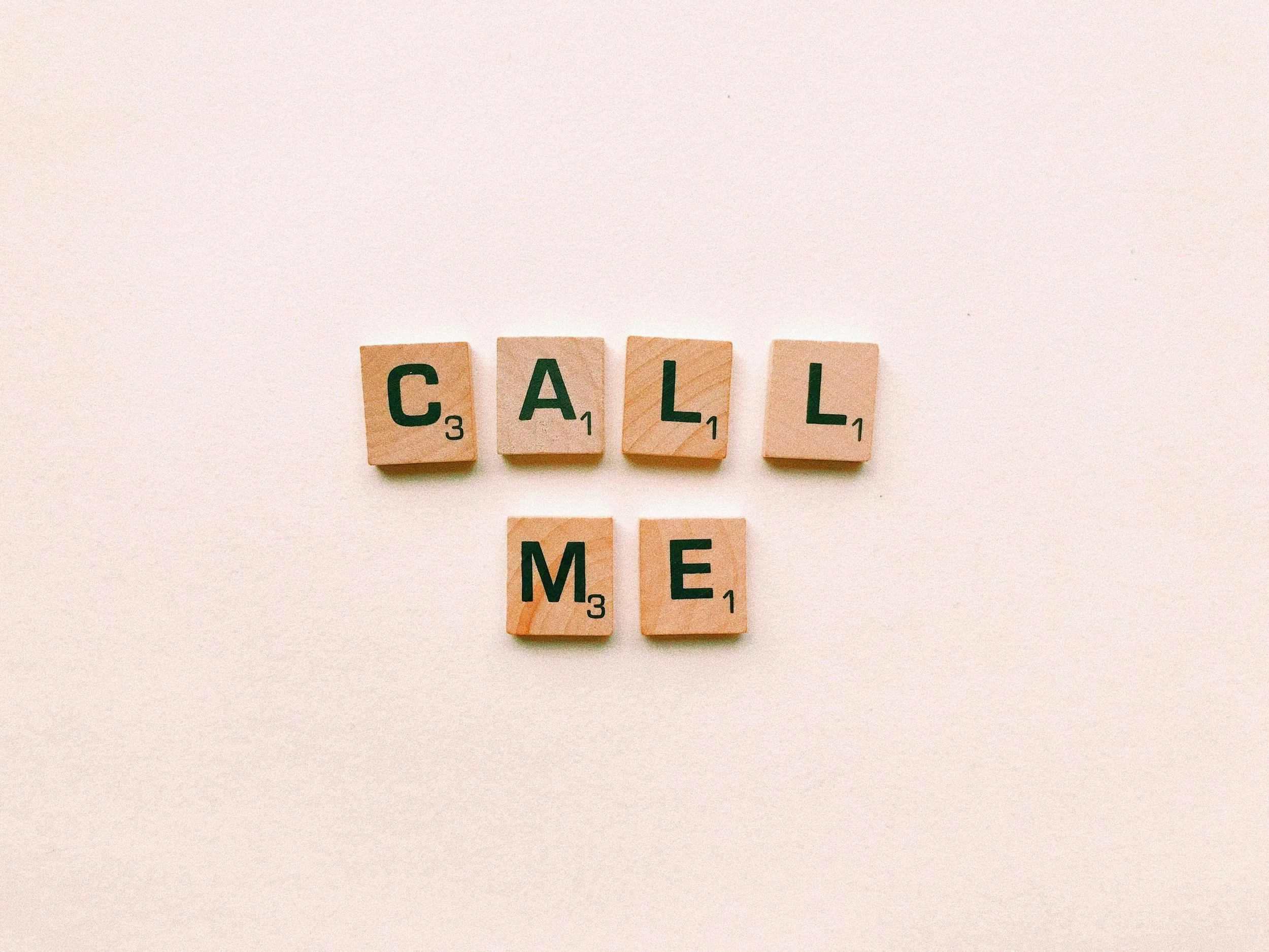 Scrabble tiles spelling out the words 'CALL' and 'ME' on a light background.