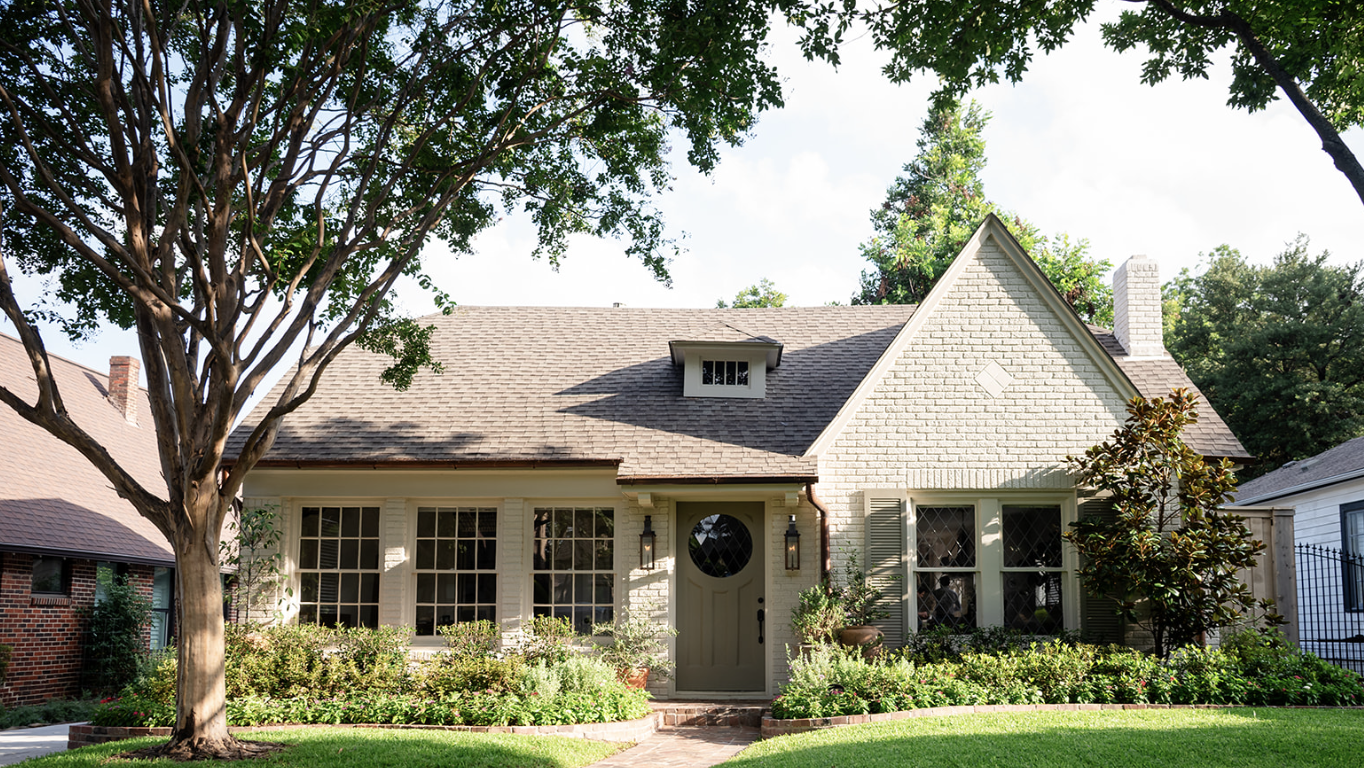 Front view of a house with a manicured lawn, trees, and shrubs, featuring a front door with lanterns on either side.