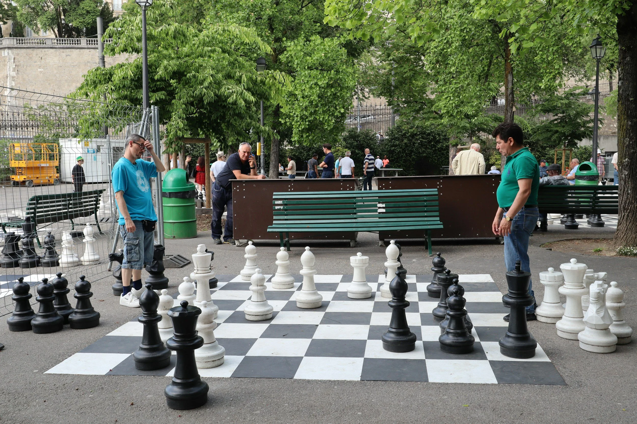 two men playing life-sized chess in the park while other people look on