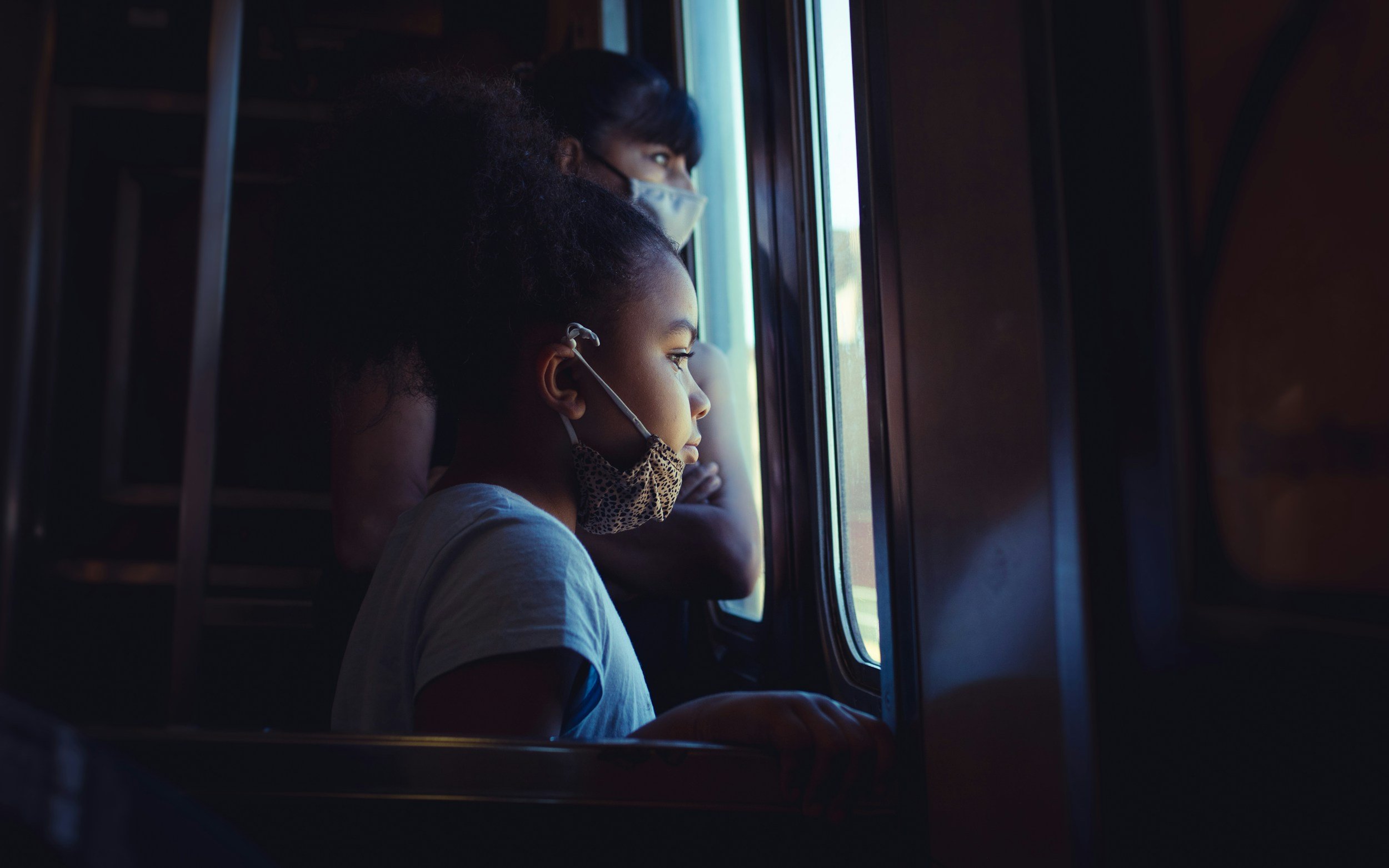 child wearing a mask looks out the subway window in NYC