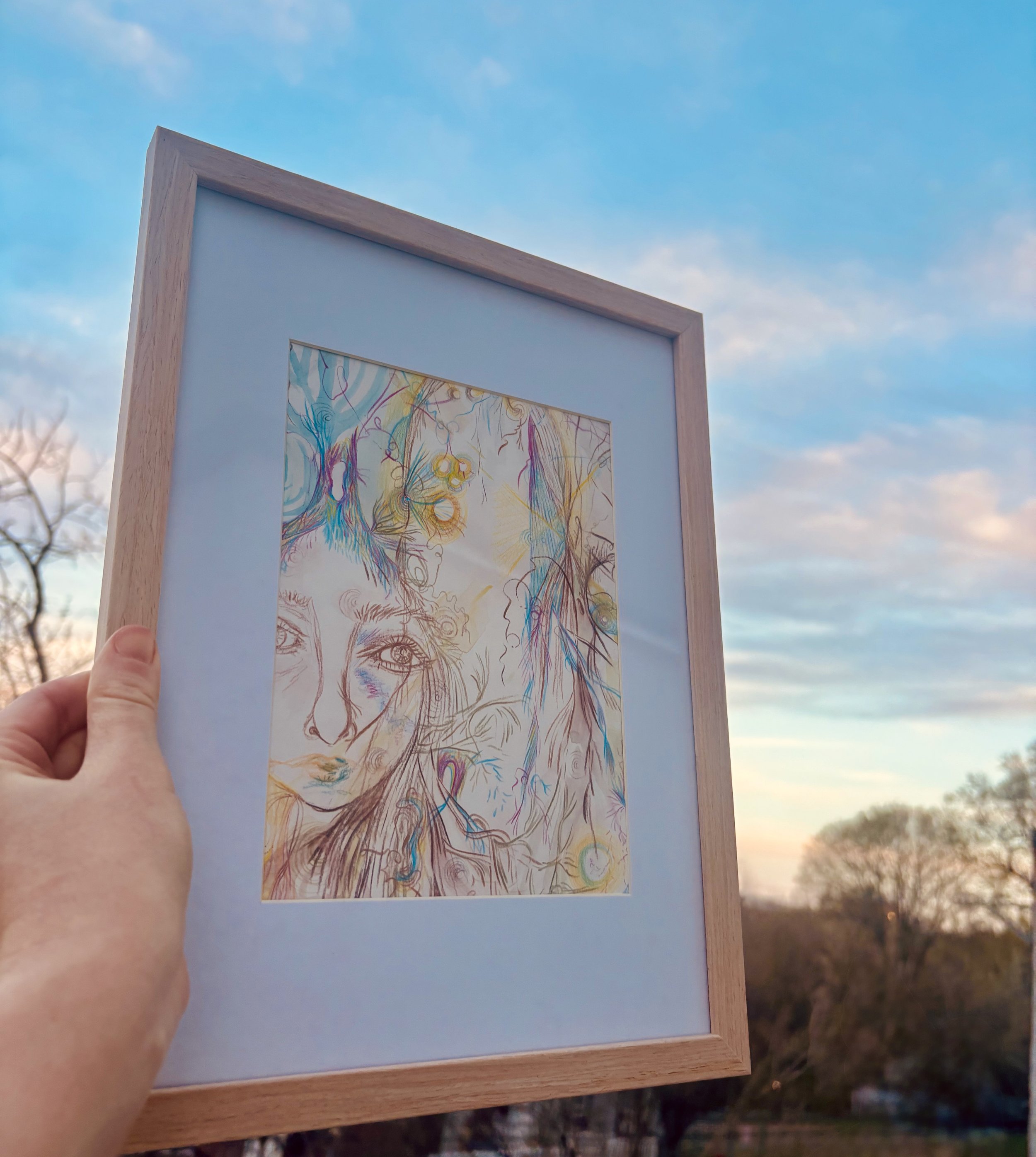 a hand gently holding "The Only Way is Through" framed mixed-media painting outdoors, illuminated by the soft glow of a sunset in the background