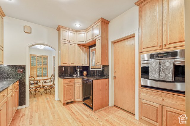 Kitchen with wooden cabinets, black countertops, and a black dishwasher. There is a built-in oven and a door to a pantry. A small window is above the sink, and a dining area is visible through an archway.