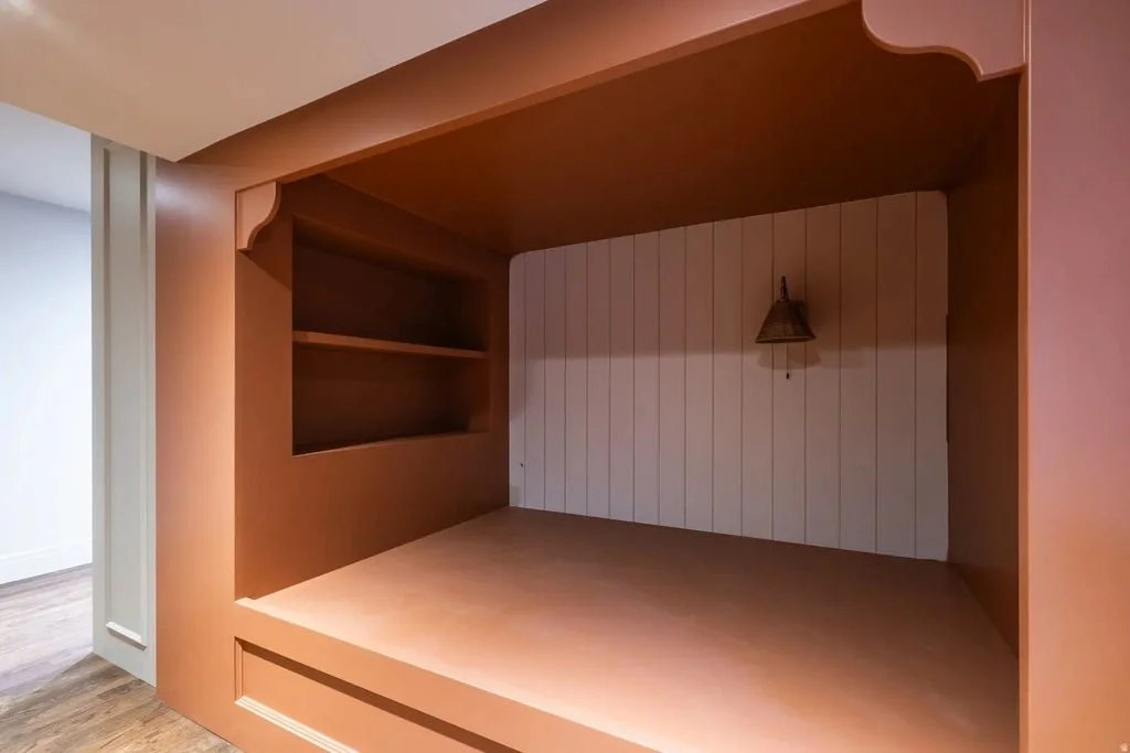 Empty built-in bed nook with a small wall lamp and storage shelf inside.
