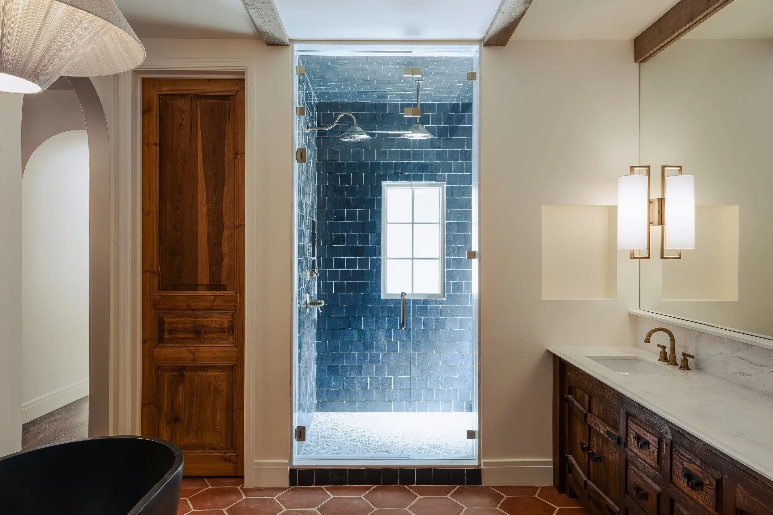Bathroom with a walk-in shower featuring dark blue tiles, a small window, wooden cabinetry, and modern lighting fixtures.