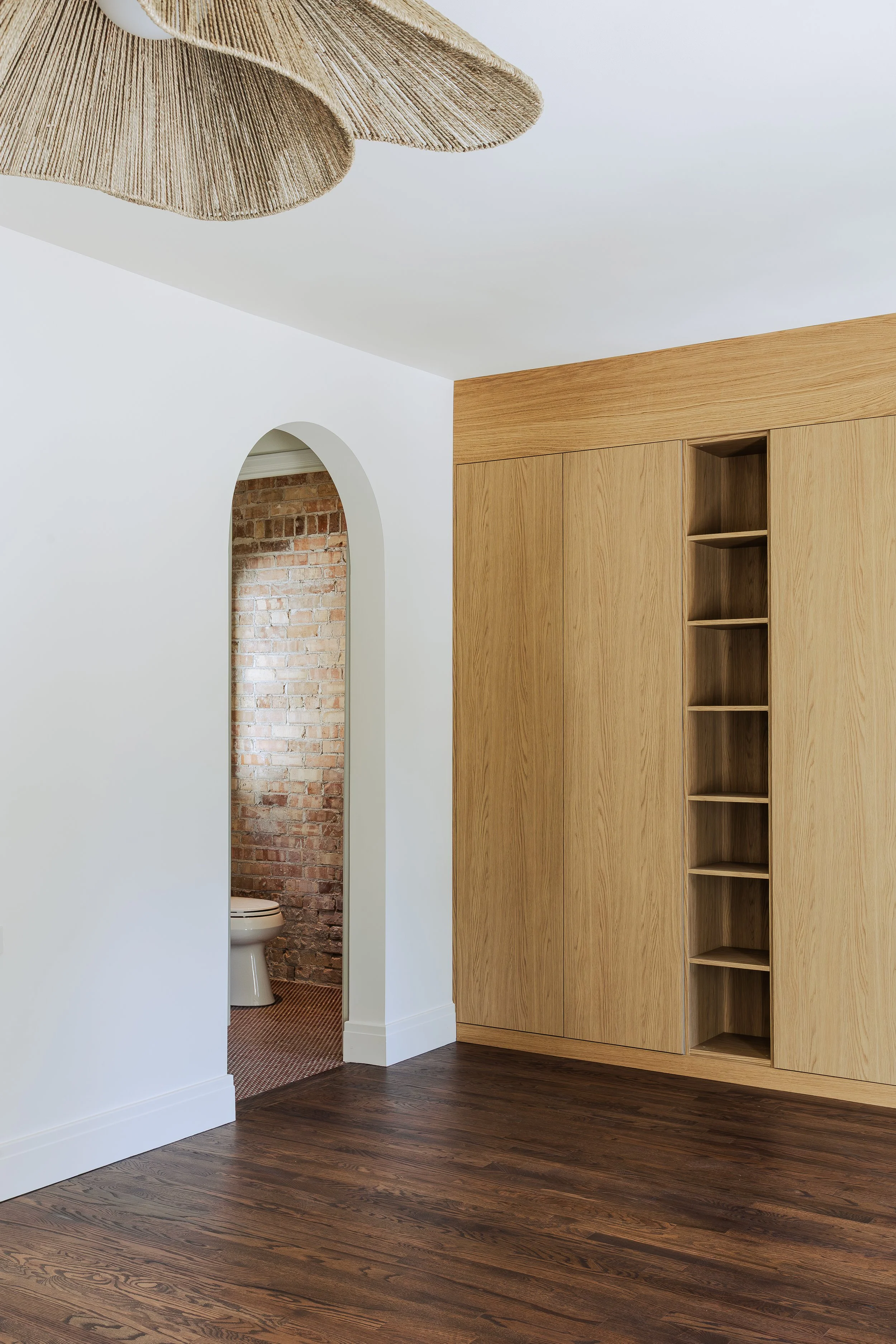 Interior room with white walls, wooden cabinetry, and a view into a small bathroom with exposed brick wall and a toilet.