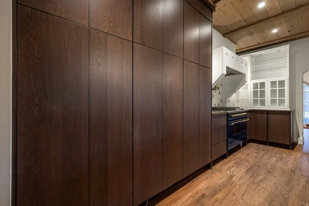 Kitchen with wooden cabinets, hardwood floor, and white ceiling, featuring a blue stove and white upper cabinets with glass doors.