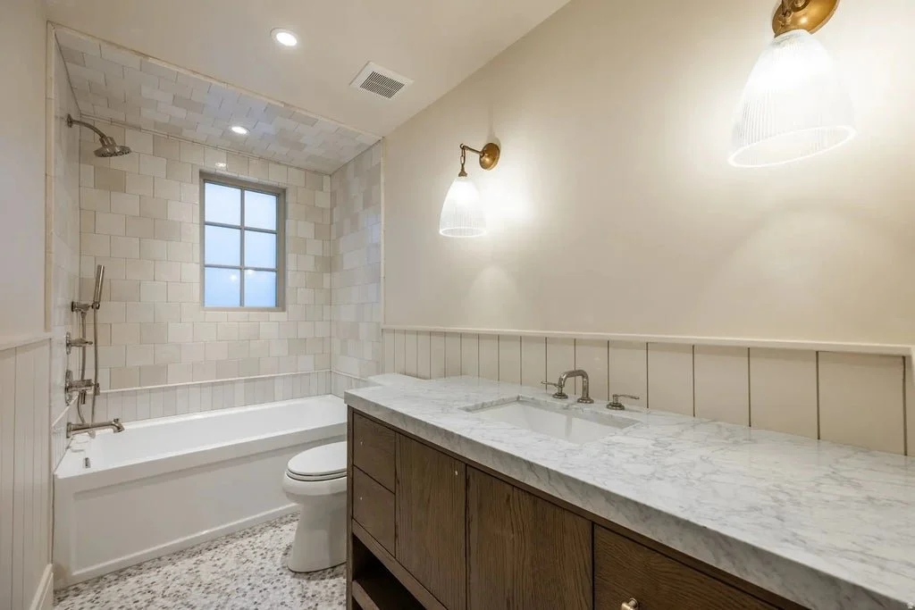 Bathroom with a bathtub, shower, window, toilet, and a marble countertop vanity with a sink.