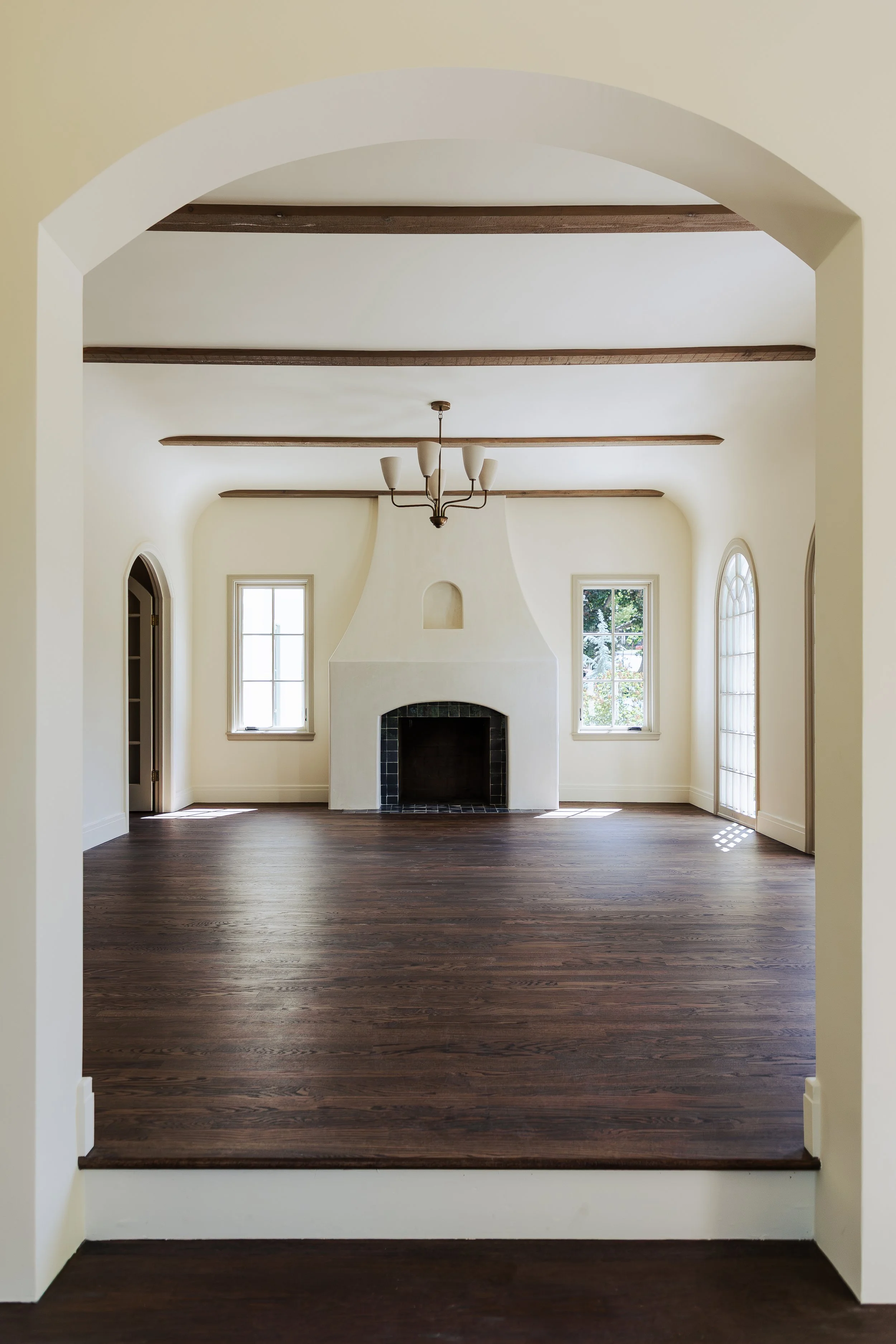 Empty living room with white walls, large windows, a fireplace, and dark hardwood flooring.