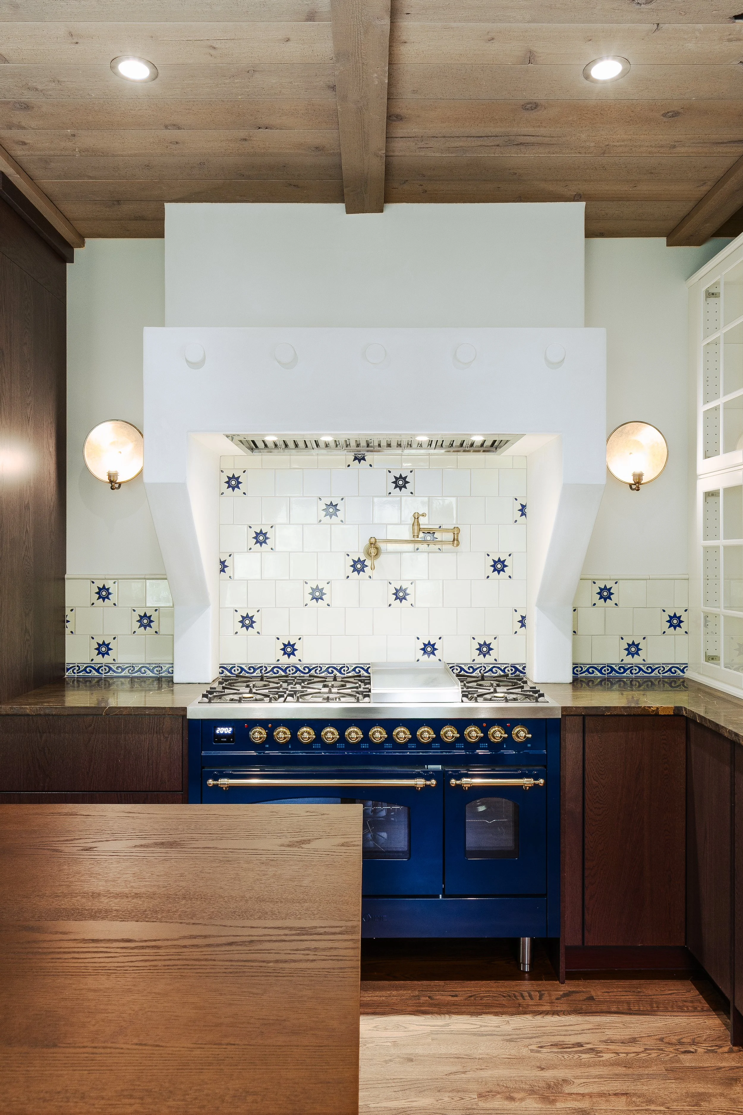 Kitchen with a blue stove, white tiled backsplash with blue star patterns, wooden cabinets on both sides, and a wooden ceiling with two recessed lights.