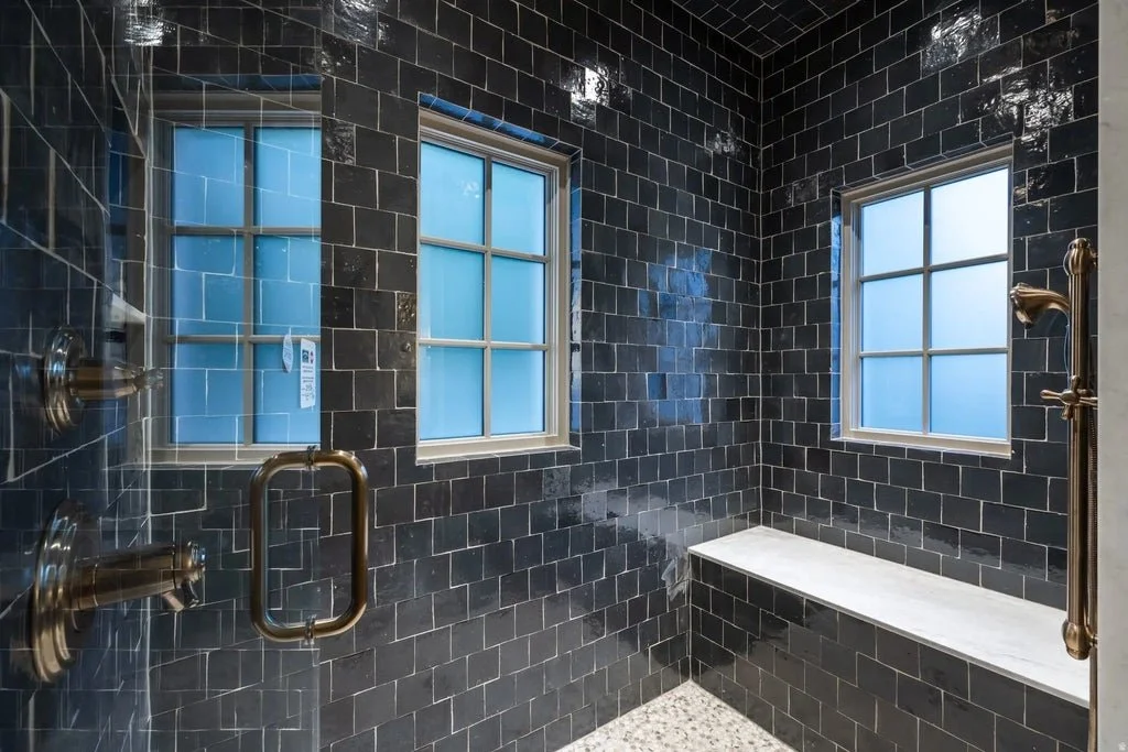 A modern, black-tiled shower with two windows, each with frosted glass, and a marble bench.