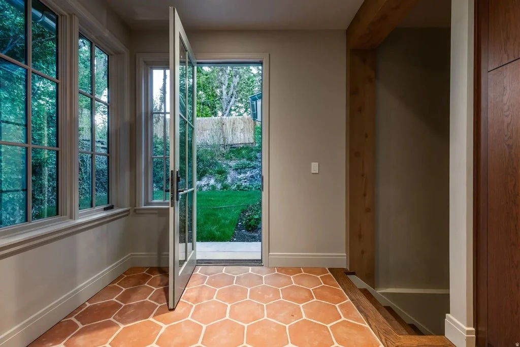 Indoor room with large windows and glass door opening to a backyard with grass and trees.