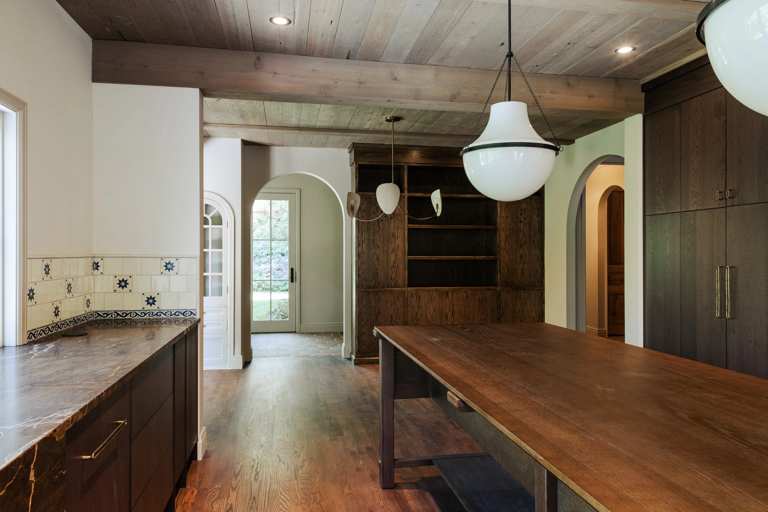 Interior of a kitchen with wooden ceiling and cabinets, white walls, a door with glass panels, and a wooden island with a thick marble countertop.
