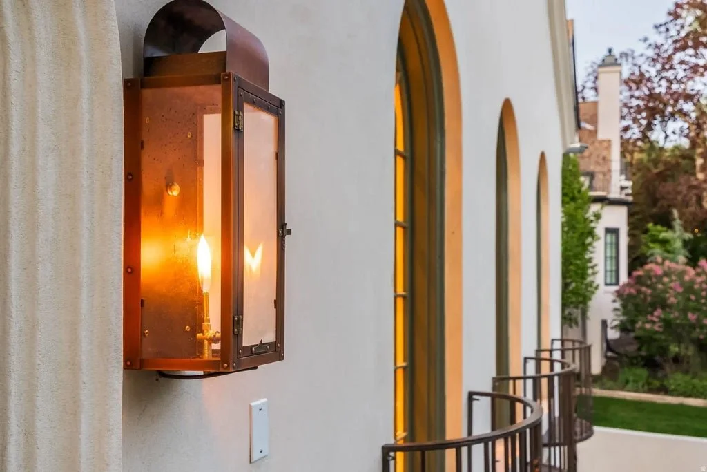 Exterior wall of a building with three arched windows and a vintage outdoor light fixture on the wall.