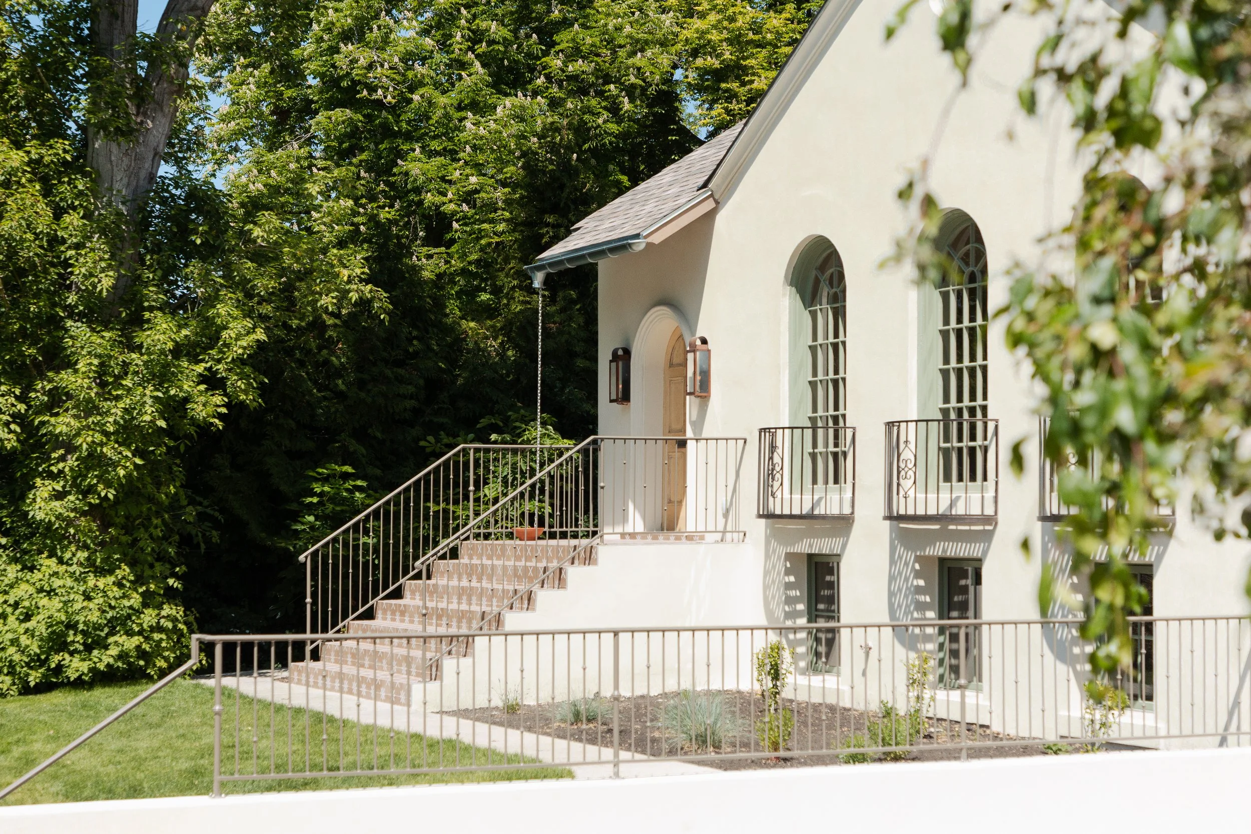 White house with arched windows, outside staircase, surrounded by green trees and a lawn.