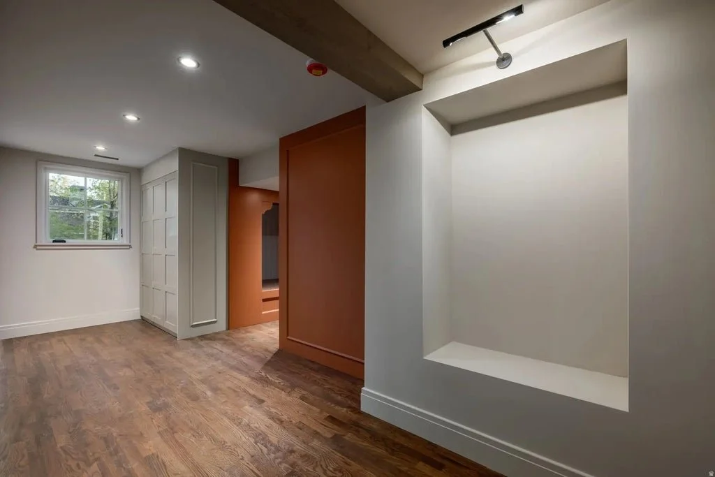 Empty corner with white walls, a built-in niche, wooden flooring, a window, and ceiling lights in a modern room.