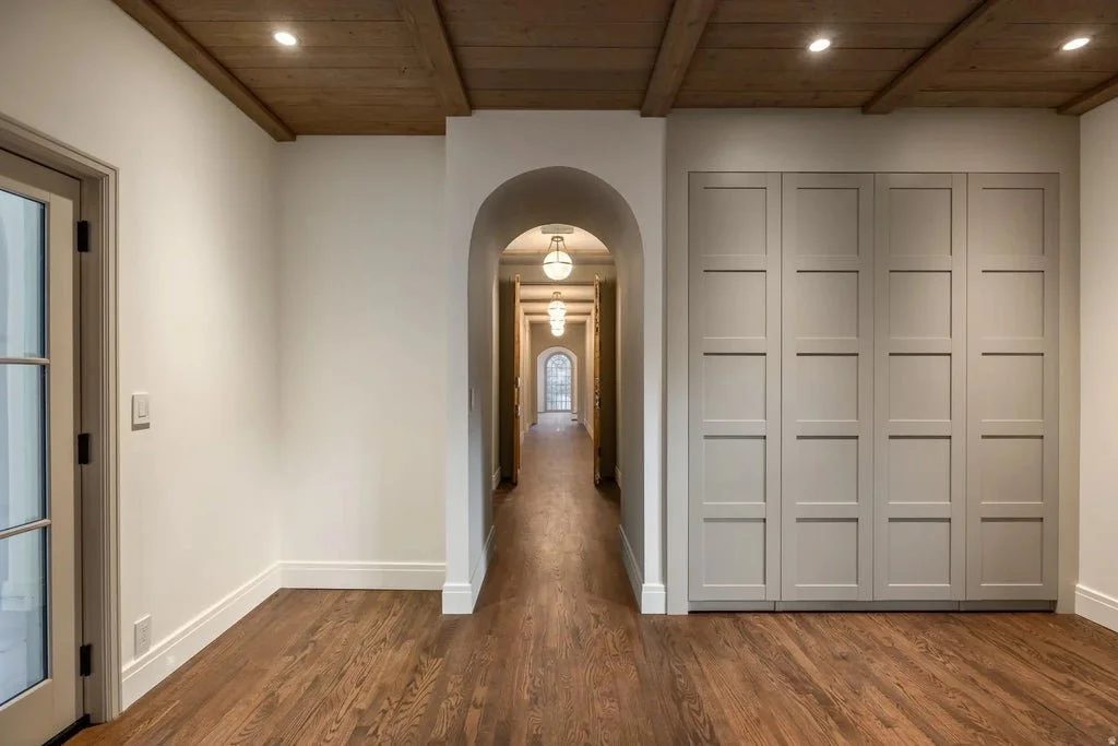 Empty room with wood flooring, white walls, a wooden ceiling, an arched doorway, and built-in closet doors.