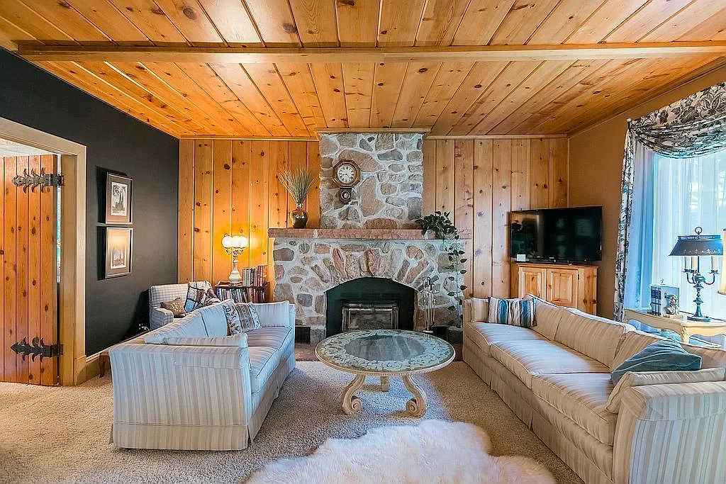 Living room with wooden ceiling and walls, stone fireplace, two striped sofas, a coffee table, and a television in a wooden cabinet.