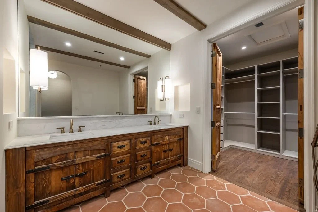 Bathroom vanity with double sinks and a large mirror, adjacent walk-in closet with shelves and hanging space.