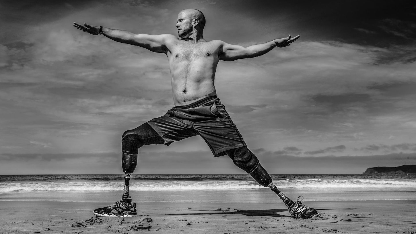Dan Nevins doing yoga on the beach with arms extended and looking to the right, ocean waves in the background, in black and white.