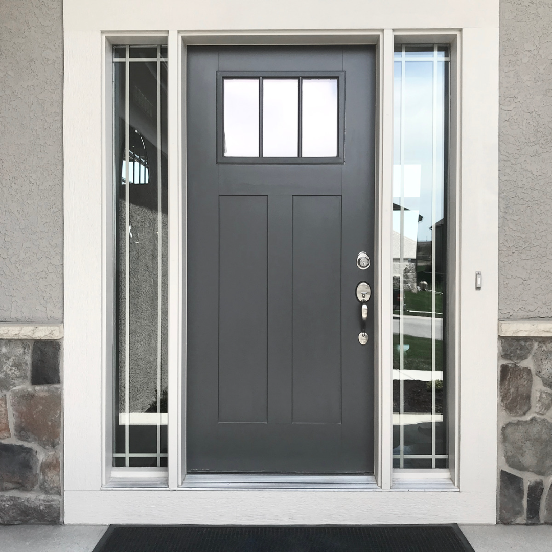Front door of a house painted dark gray, with a rectangular window at the top and side glass panels with metal bars, framed by white trim, on a house with beige textured walls and stone accents.